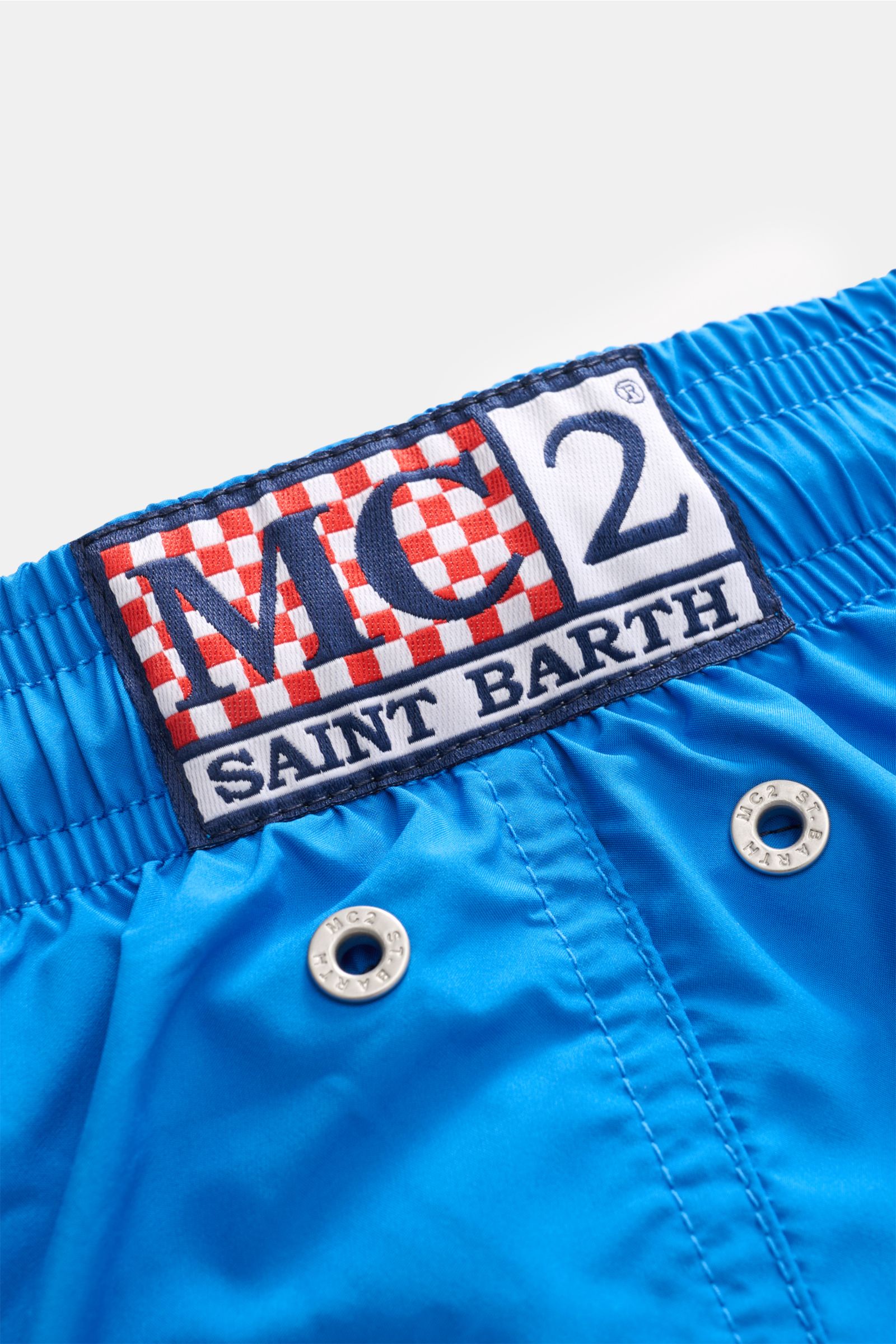 Nahaufnahme der elastischen Taille der MC2 Saint Barth Badeshorts 'Lightning Pantone' blau mit gesticktem Label und Metall-Ösen, Perspektive von oben.