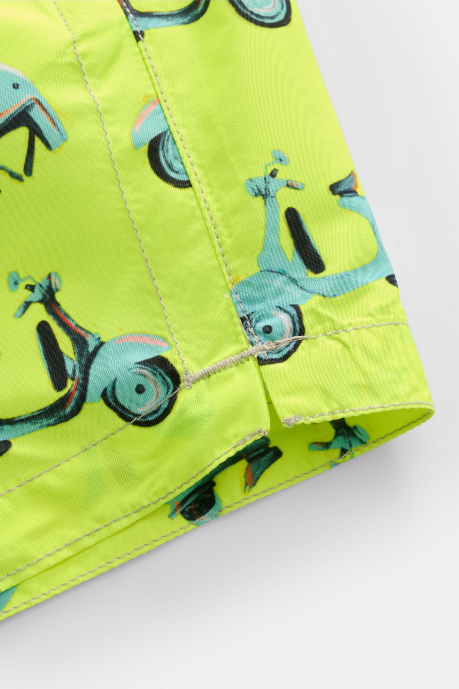 Close-up view of the hem and side seam of Zeybra Portofino 1962 Badeshorts 'Scooter' neongelb/hellblau gemustert with a neon yellow base and light blue scooter print. Sommerliches Statement: Mit ihrem markanten Allover-Print werden die Badeshorts von Z