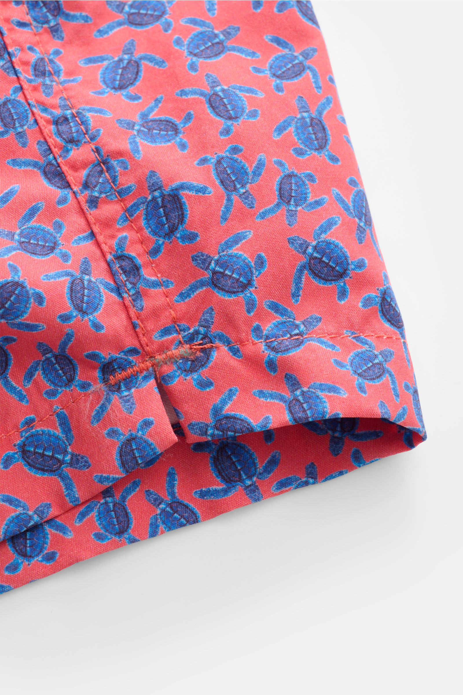 Close-up view of the hem and side seam of Zeybra Portofino 1962 Badeshorts 'Tatarughe' rot/blau gemustert with blue turtle print on red fabric. Eyecatcher für sonnige Tage: Die Badeshorts von ZEYBRA PORTOFINO 1962 überzeugen mit kurzem Schnitt und auffäll