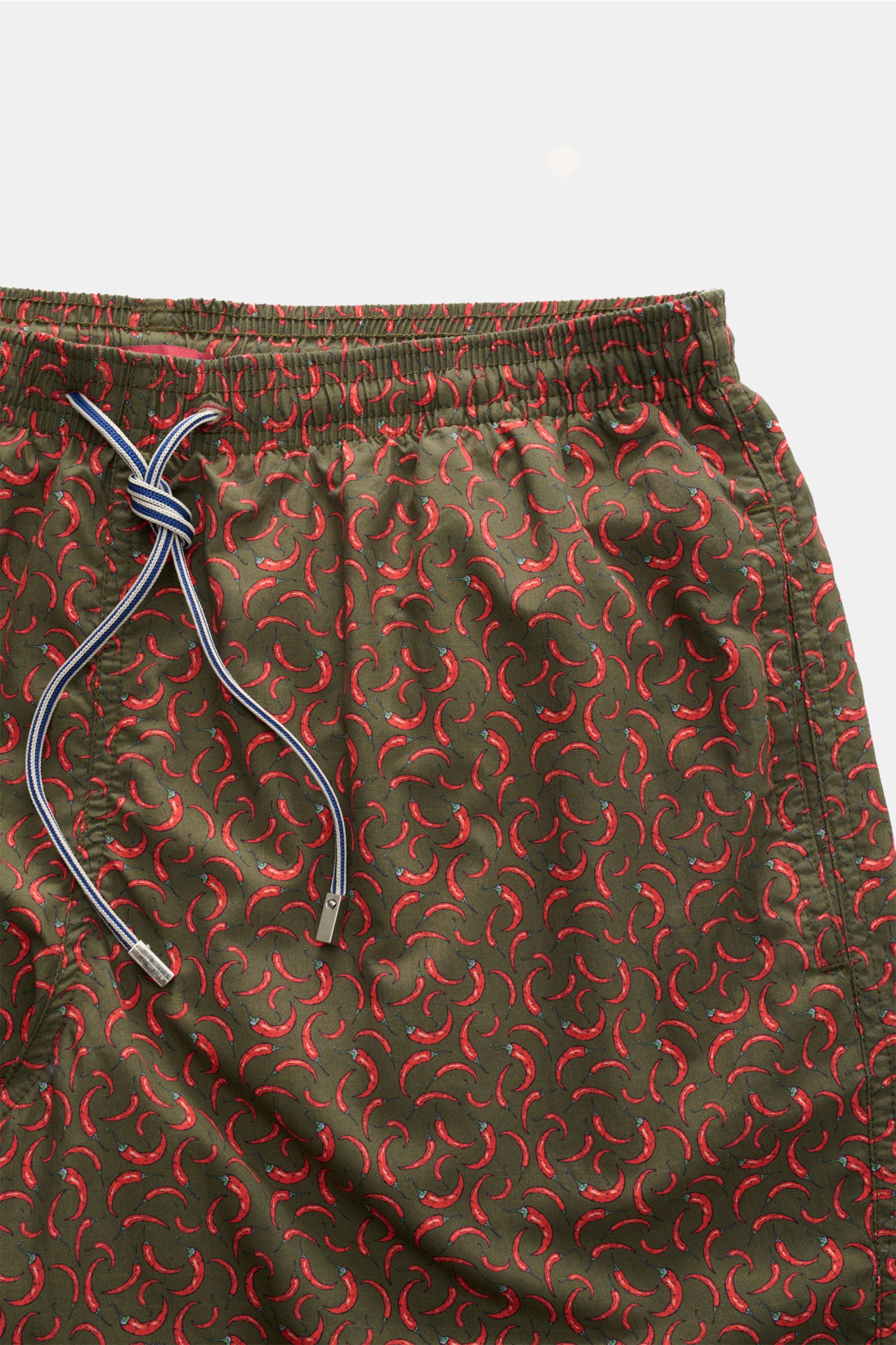 Close-up front view of Zeybra Portofino 1962 Badeshorts 'Peperoncini' dunkelgrün/rot gemustert with elastic waistband, drawstring, and red chili pepper print. Eyecatcher für sonnige Tage: Die Badeshorts von ZEYBRA PORTOFINO 1962 überzeugen mit kurzem Schn
