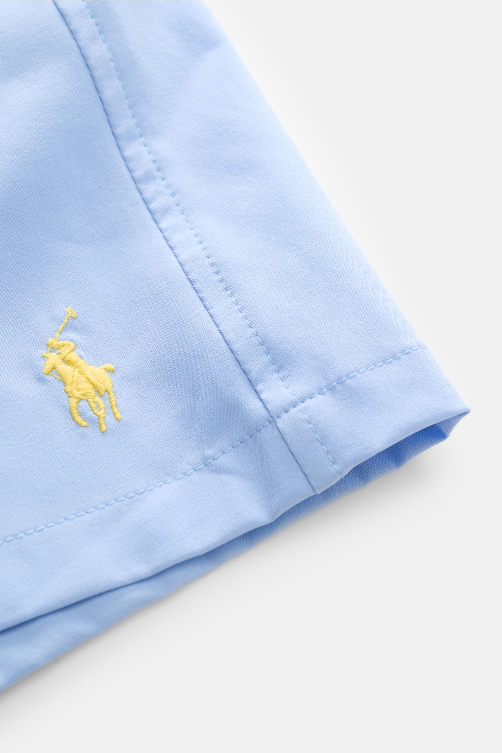 Nahaufnahme der Polo Ralph Lauren Badeshorts 'Traveler' hellblau von schräg oben, zeigt feine Naht, gelbes Logo-Stitching, schnelltrocknende Microfaser.