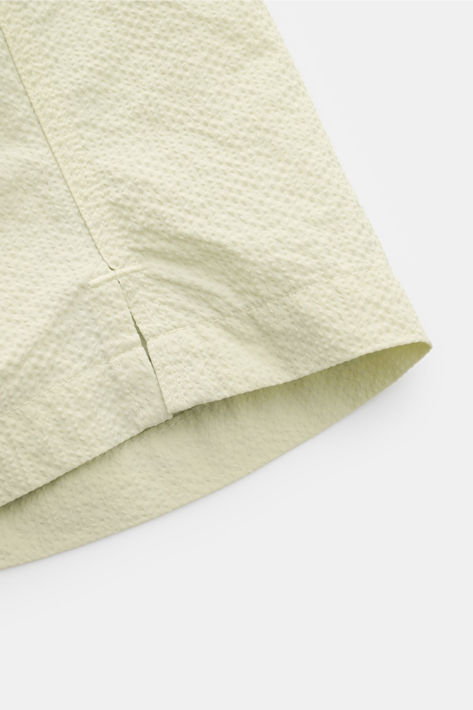 Nahaufnahme der seitlichen Saumschlitze der 04651/ A trip in a bag Badeshorts 'Mono Seersucker' salbei aus leichtem Seersucker-Microfaserstoff.