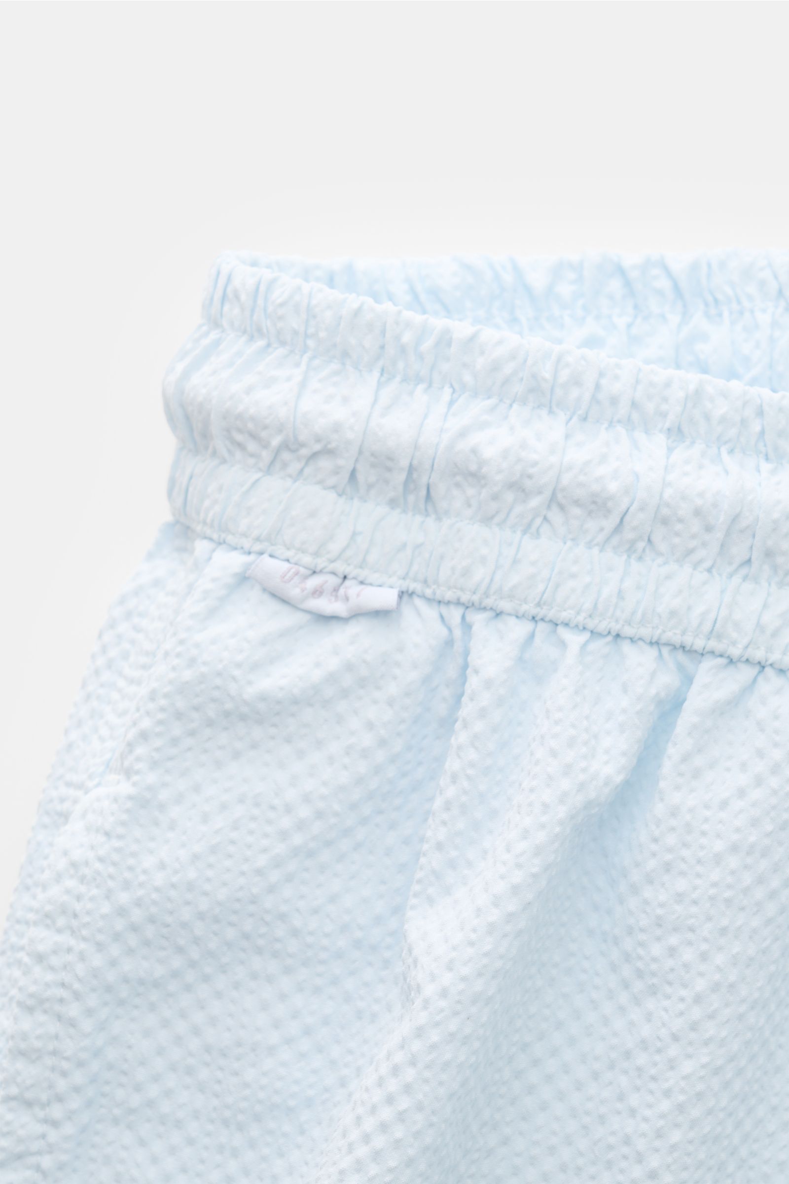 04651/ A trip in a bag Badeshorts 'Mono Seersucker' pastellblau in Nahaufnahme von oben mit elastischem Bund, Seersucker-Microfaser und leichtem Griff.