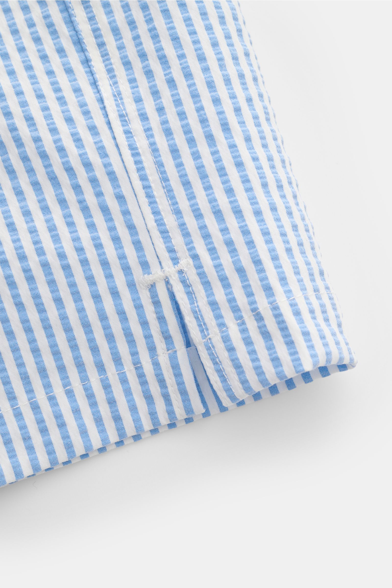 Close-up view of the hem with side vents of the 04651/ A trip in a bag Swim shorts blue/white striped, showing the seersucker fabric texture and vertical stripes. 

Perfect for your next summer holiday: With their modern striped pattern, these swim sho