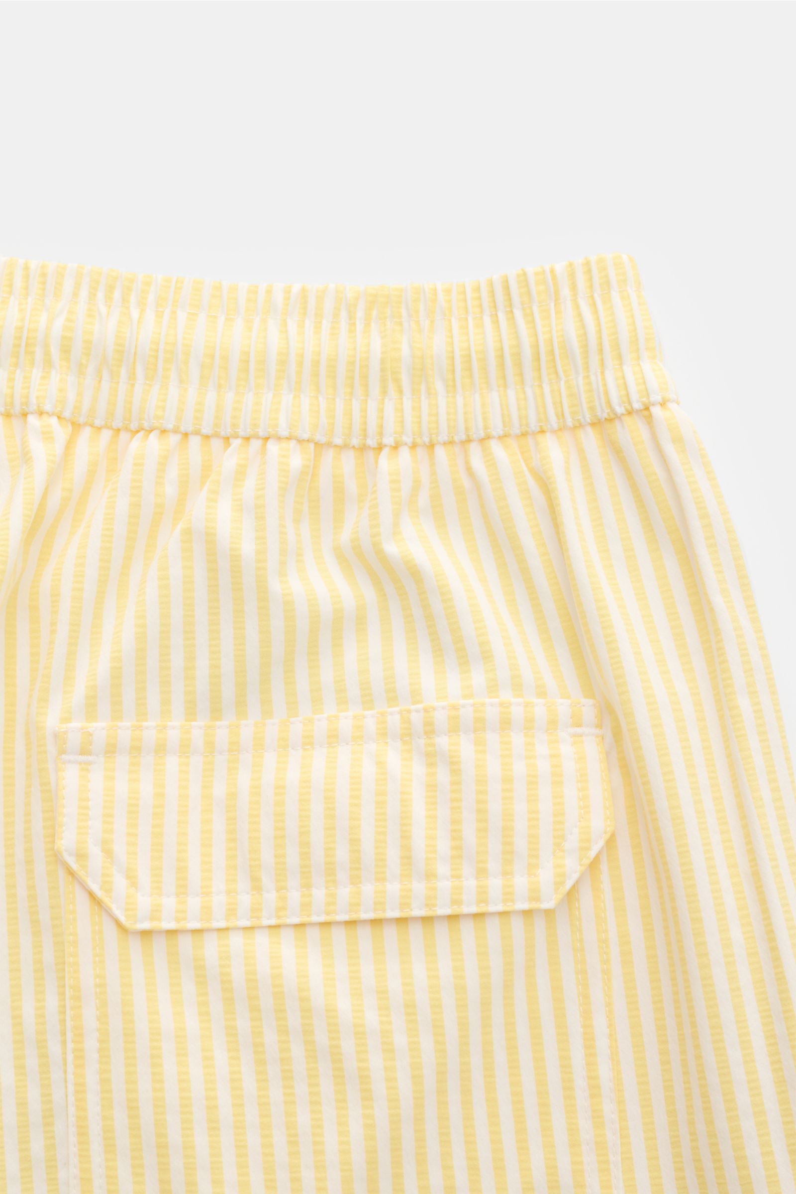 Close-up rear view of 04651/ A trip in a bag swim shorts pastel yellow/white striped with elastic waistband and back pocket.

Perfect for your next summer holiday: With their modern striped pattern, these swim shorts by 04651/ A TRIP IN A BAG are an ey