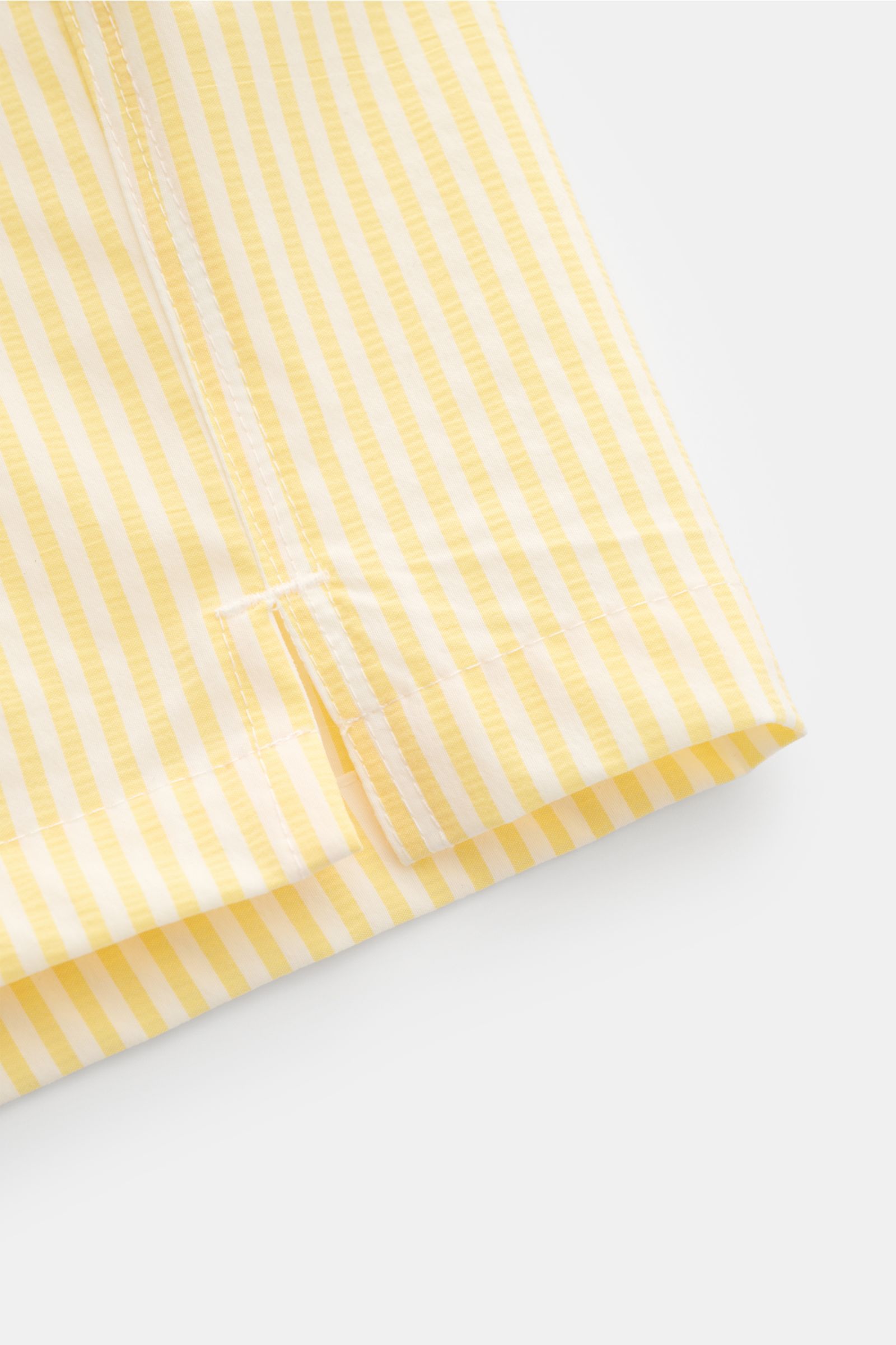 Close-up from a side angle of 04651/ A trip in a bag Swim shorts pastel yellow/white striped hem with side vents showing striped seersucker fabric.

Perfect for your next summer holiday: With their modern striped pattern, these swim shorts by 04651/ A 