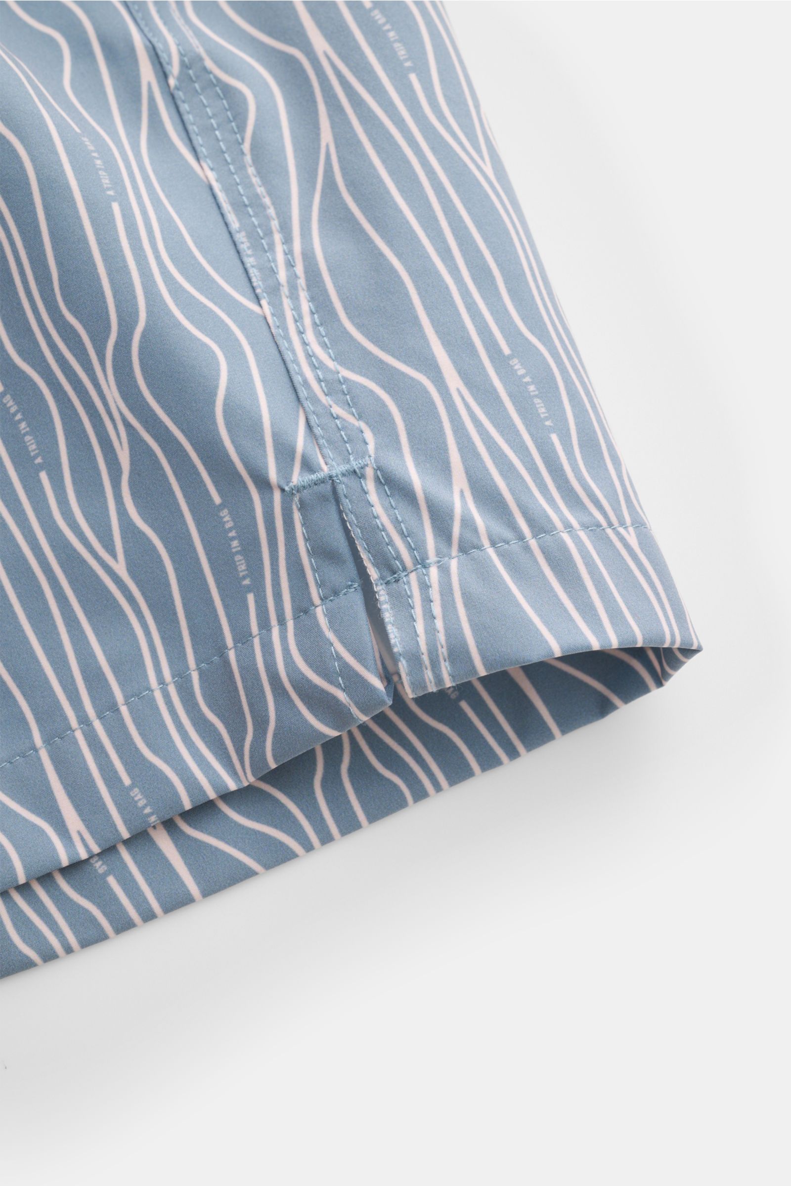 Close-up side view of 04651/ A trip in a bag Swim shorts 'Superkilen' smoky blue/white patterned hem with side vents and stitching details.

An eye-catching piece for summer: With their all-over print inspired by Copenhagen’s 'Superkilen' park, these s