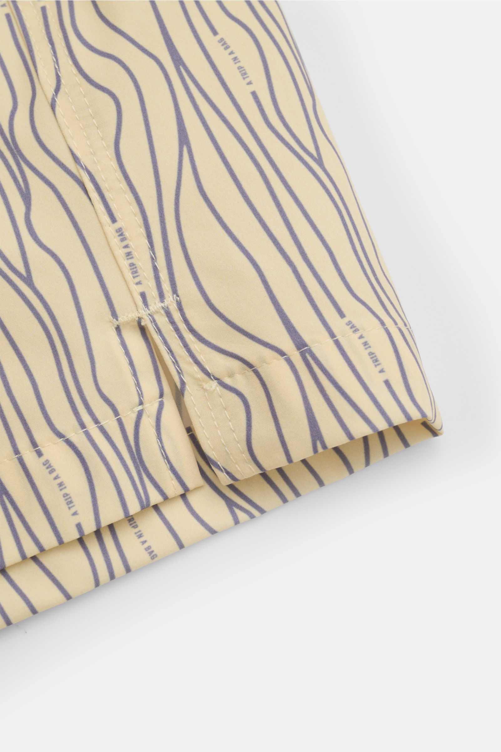 Close-up side view of 04651/ A trip in a bag Swim shorts 'Superkilen' pastel yellow/lavender patterned hem with side vents and wavy print.

An eye-catching piece for summer: With their all-over print inspired by Copenhagen’s 'Superkilen' park, these sw