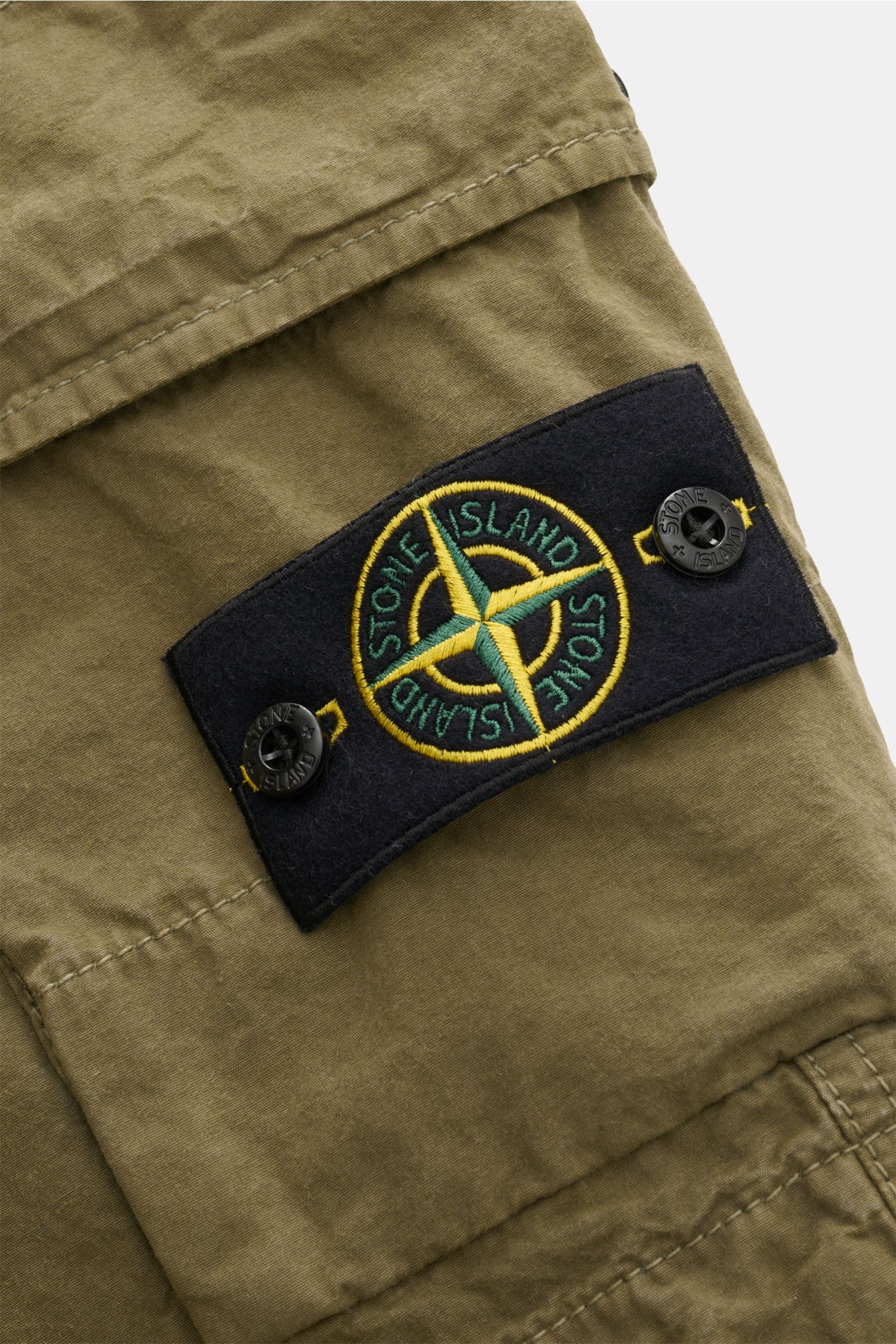 Nahaufnahme der Stone Island Cargo-Bermudas oliv mit markentypischem Kompass-Badge, weichem Baumwollstoff und Cargotasche.