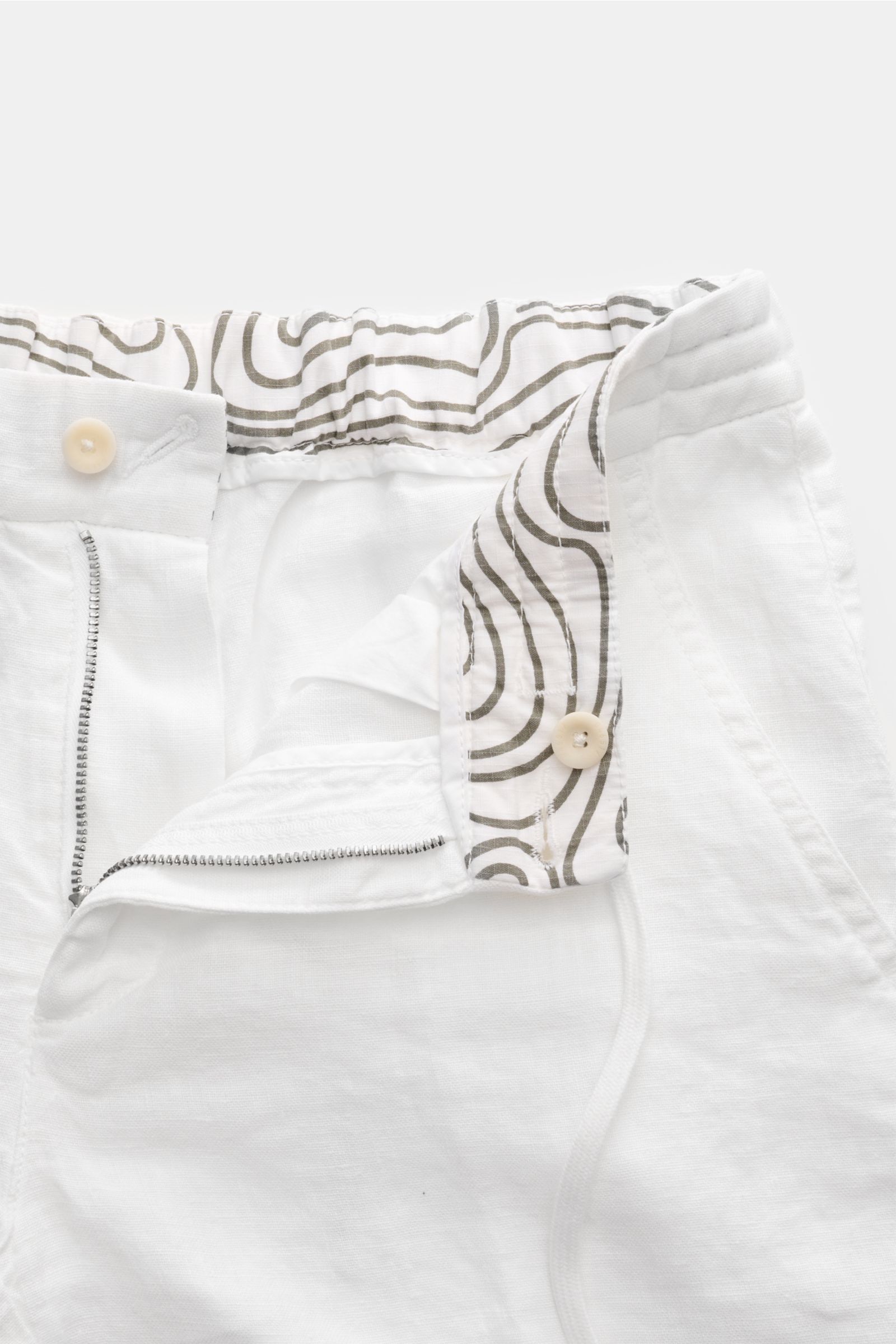 Close-up front view of 04651/ A trip in a bag Linen bermudas 'Linen Bermuda' white showing elasticated waistband with drawstring, zip, button, and patterned inner lining.

These airy Bermudas by 04651/ A TRIP IN A BAG are a must-have for your next beach h