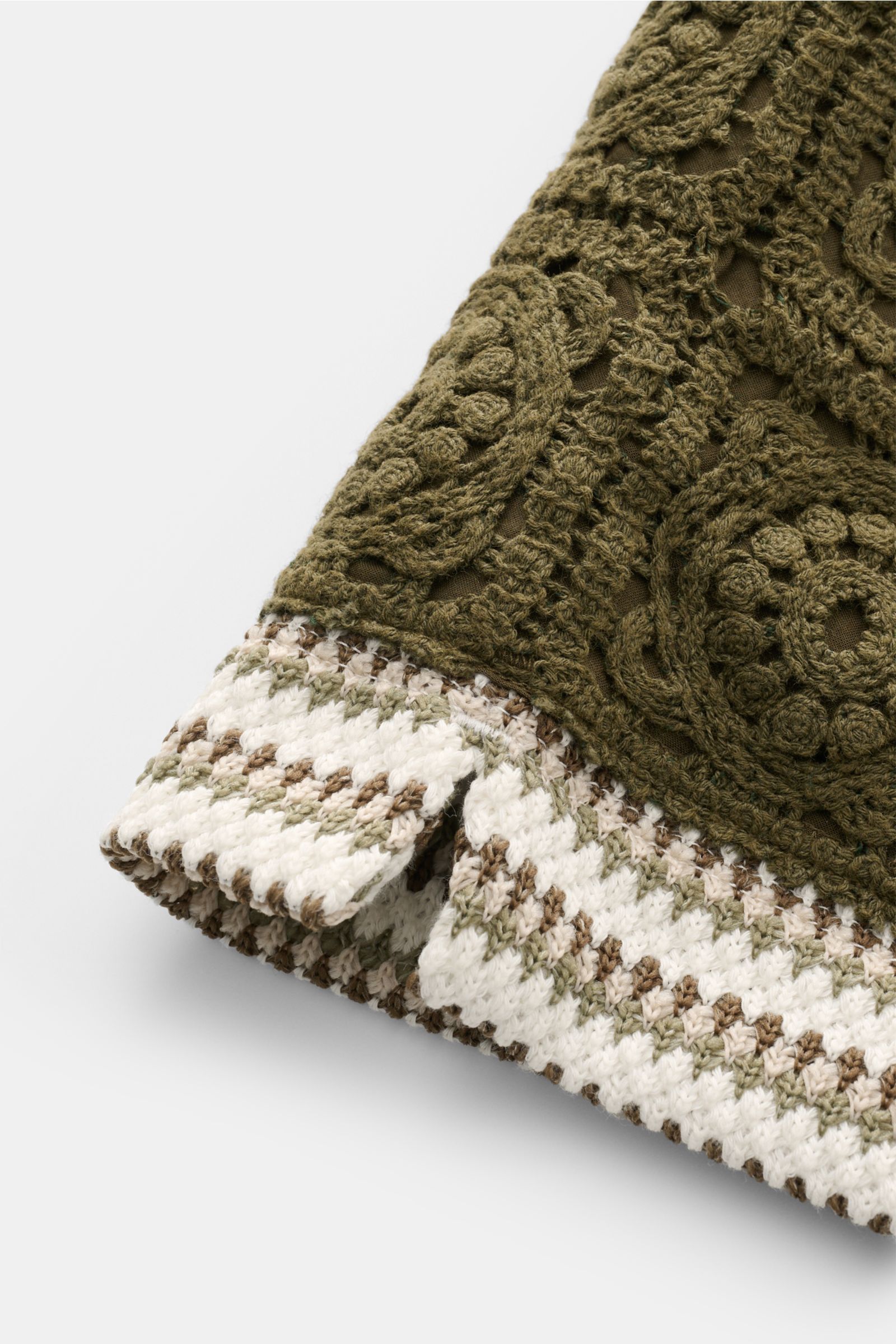 Nahaufnahme der Ché Shorts 'Mathias' creme/salbei/dark olive gestreift in leichter, feiner Strickstruktur mit aufgesetzter Häkel-Tasche, fotografiert aus schräger Perspektive.