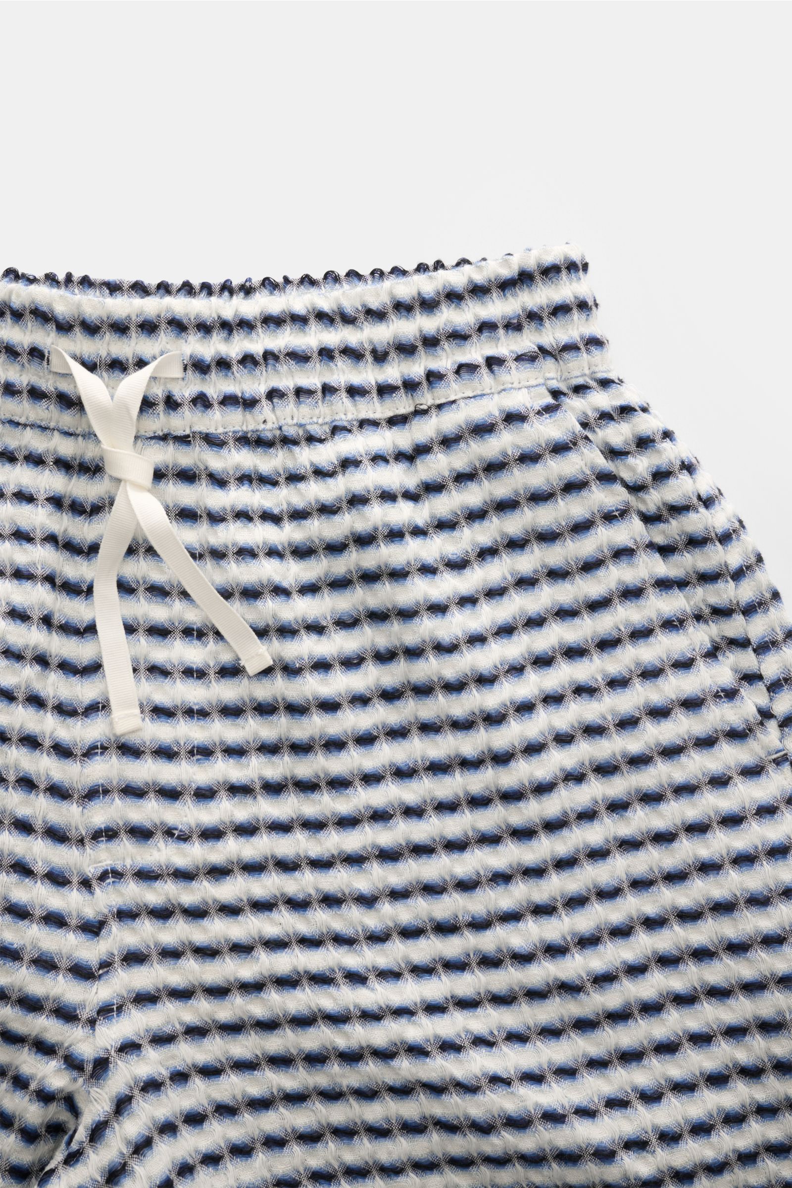 Nahaufnahme der Ché Shorts 'Riita' blau/weiß gemustert aus reinem Leinen mit elastischem Tunnelzugbund, Waffelpiqué-Struktur, seitlicher Tasche, frontal fotografiert.