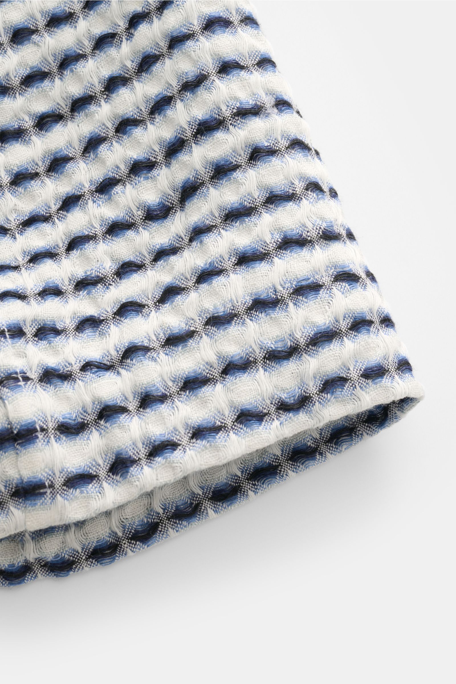Nahaufnahme der sommerlichen Ché Shorts 'Riita' blau/weiß gemustert, fotografiert von schräger Seitenperspektive, zeigt reines Leinen mit aufwändig gewebtem Waffelpiqué und grobem, luftigem Strickmuster.