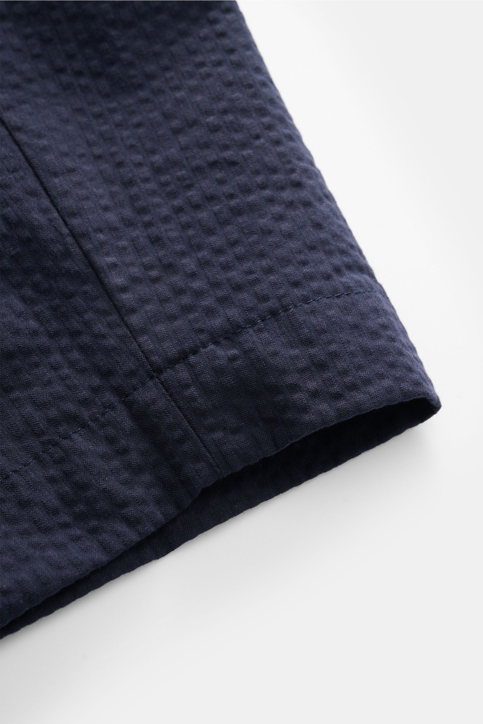 Nahaufnahme der Officine Générale Seersucker-Shorts 'Georges' navy mit typischer Baumwoll-Seersucker-Struktur, Detailansicht vom Beinabschluss.