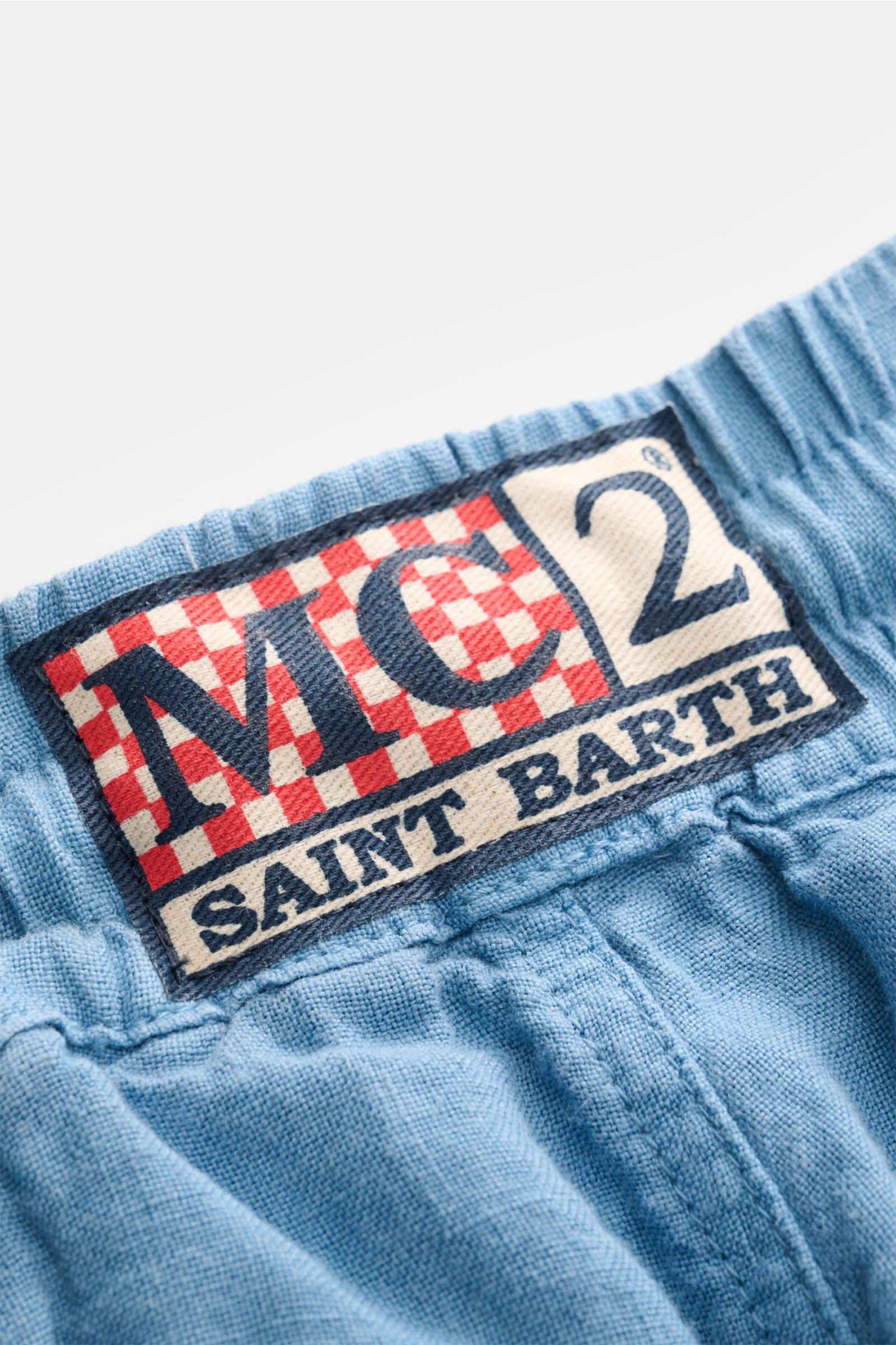 Close-up top view of the woven label on the elasticated waistband of MC2 Saint Barth Linen cargo shorts 'Marseille' smoky blue, showcasing the red and white checkered pattern, tonal stitching, and textured garment-dyed pure linen fabric.