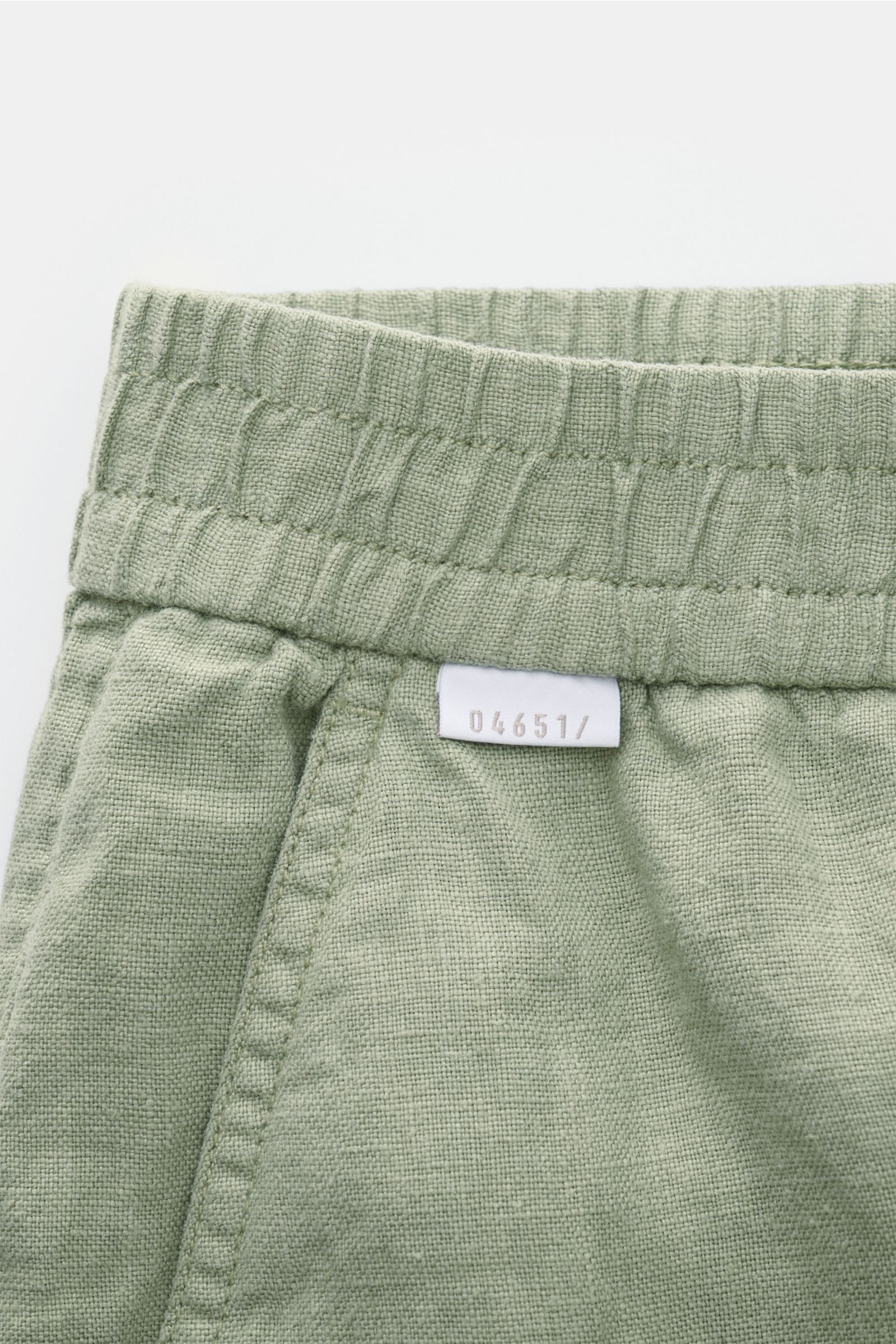 Close-up front view of 04651/ A trip in a bag Linen shorts sage showing elastic waistband, French pocket, and small woven label.

With this airy model, 04651/ A TRIP IN A BAG presents a comfortable pair of pure linen shorts that are the perfect compani