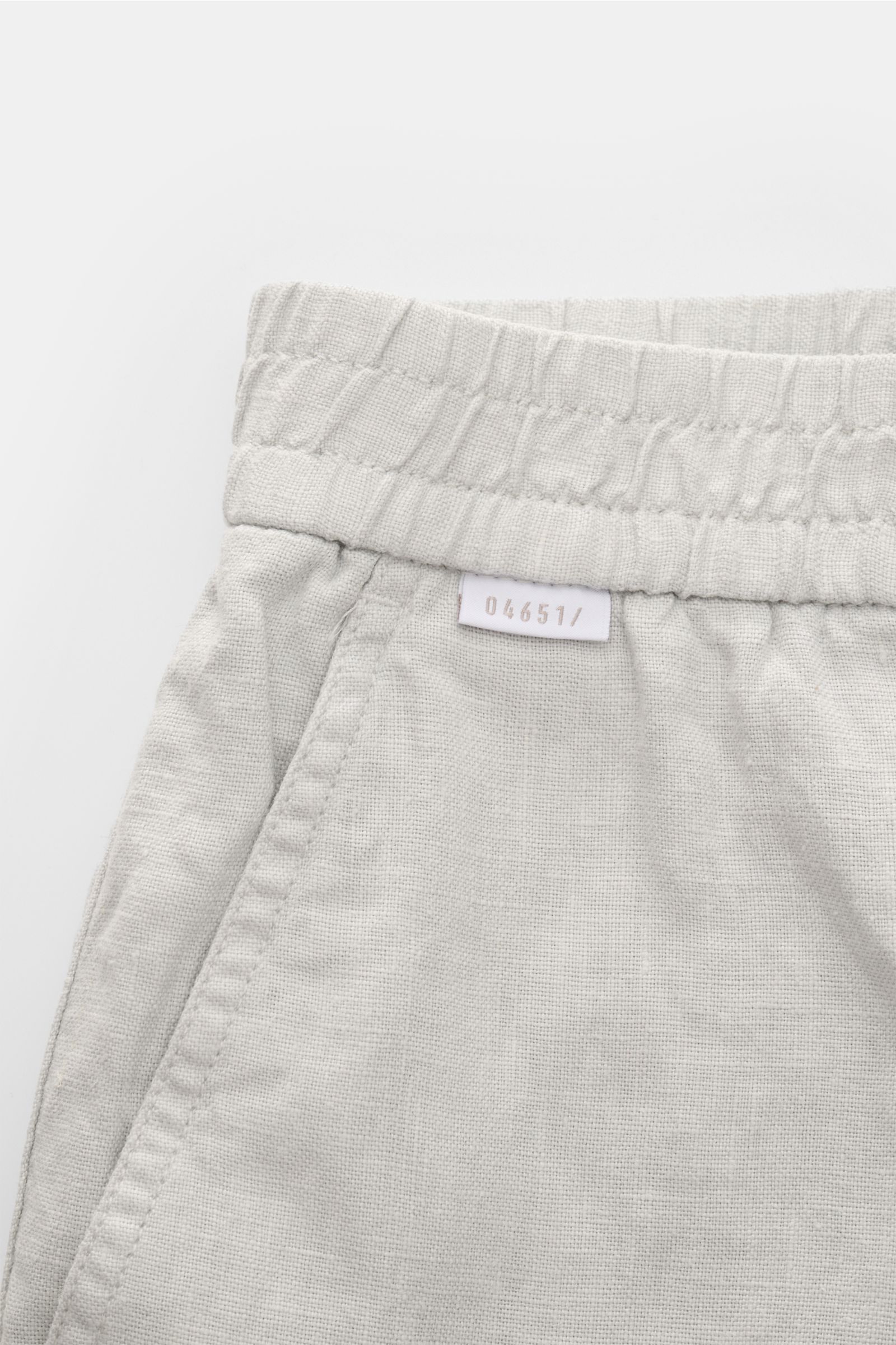 Nahaufnahme der 04651/ A trip in a bag Leinenshorts hellgrau von vorne oben, luftiges Leinengewebe, elastischer Bund, französische Taschen, kleines Weblabel am Bund.