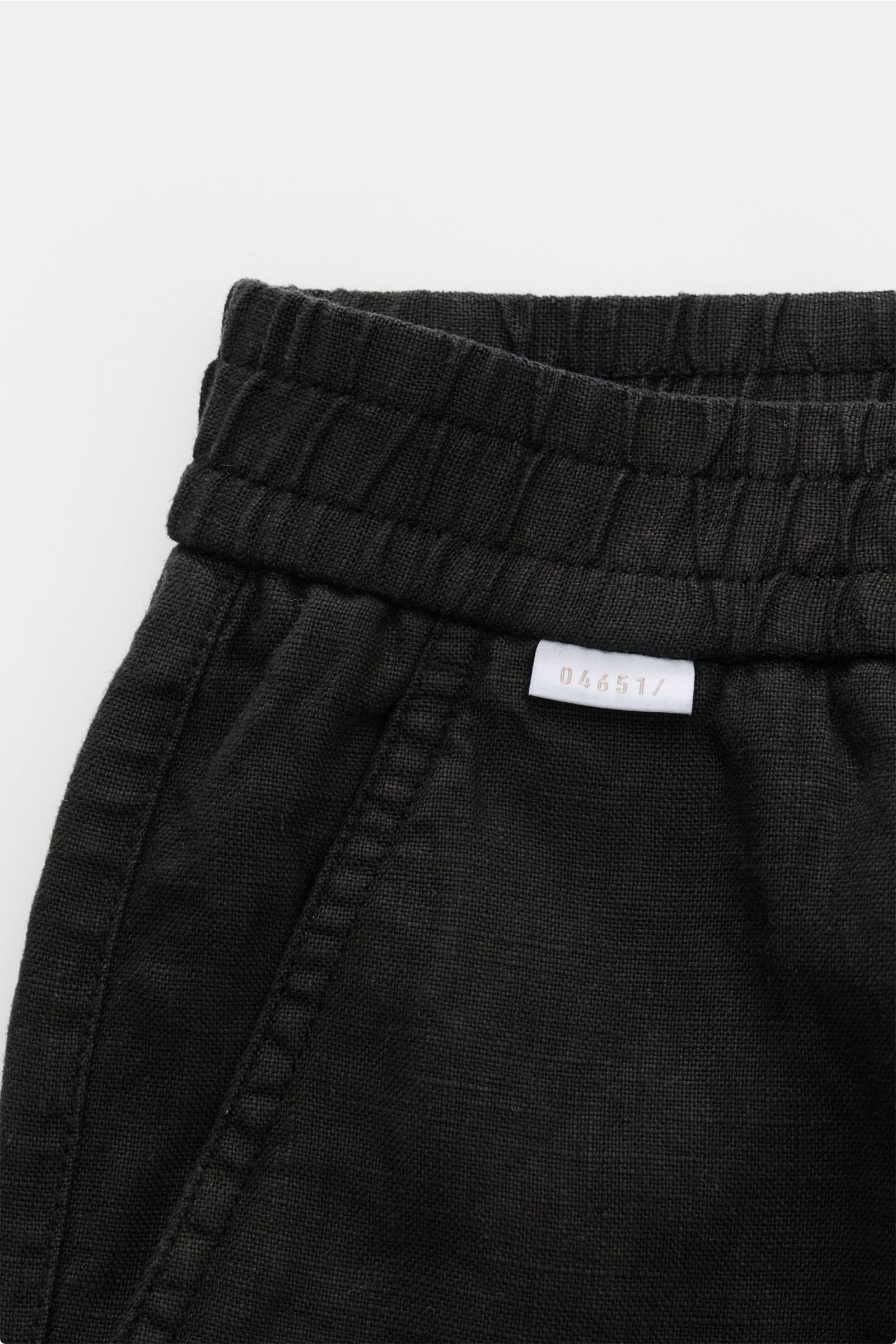 Close-up front view of 04651/ A trip in a bag Linen shorts black showing elastic waistband, French pocket, and small woven label.

With this airy model, 04651/ A TRIP IN A BAG presents a comfortable pair of pure linen shorts that are the perfect compan