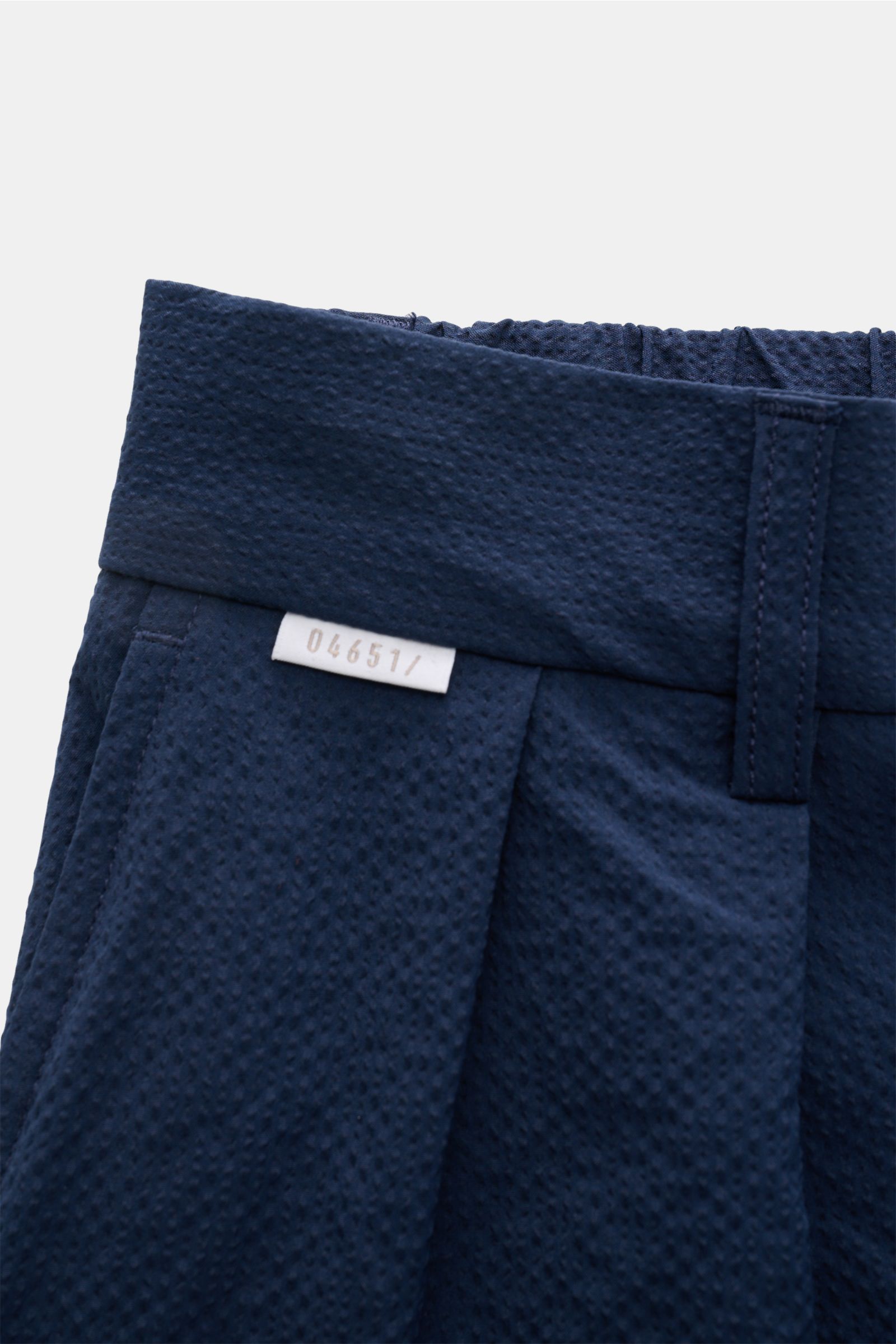 Nahaufnahme der Taille der 04651/ A trip in a bag Seersucker-Shorts navy aus strukturtypischem Microfaser-Seersucker mit teilelastischem Bund, doppelter Bundfalte und kleinem Weblabel, fotografiert von schräg vorne.