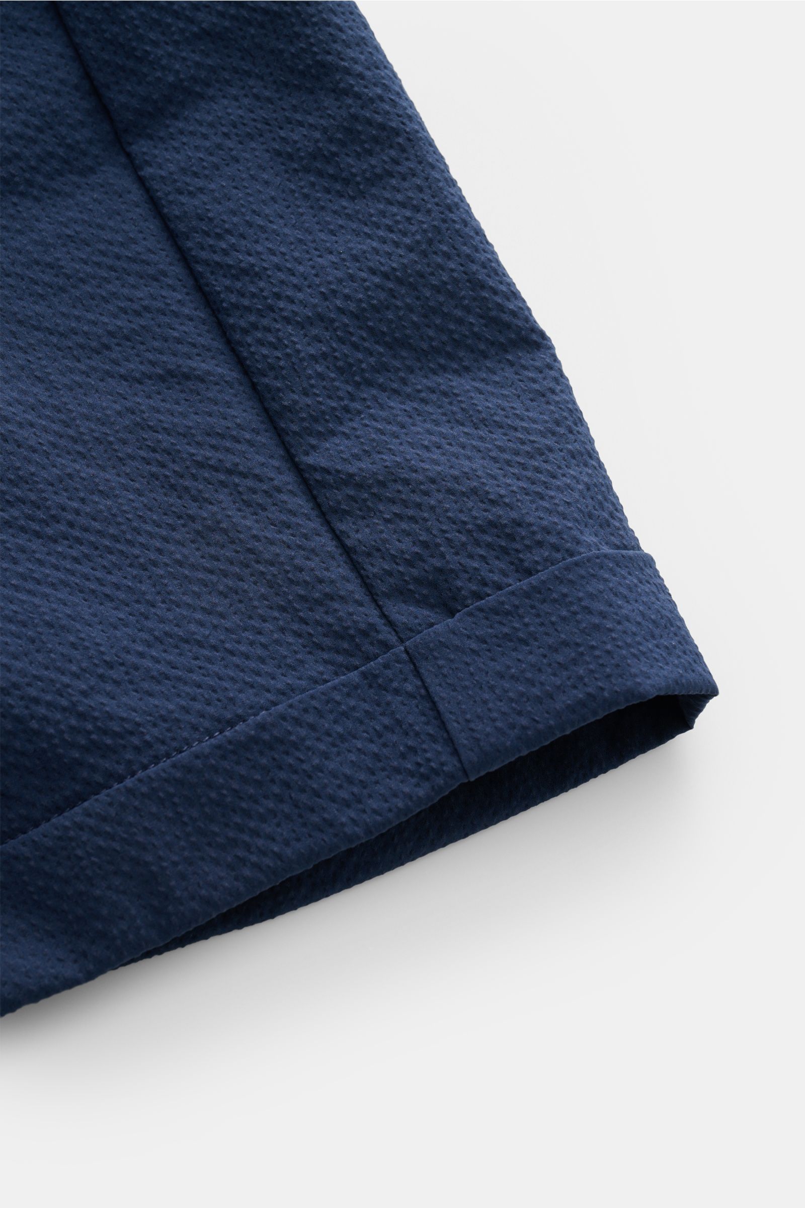 Nahaufnahme der fixierten Saumaufschläge der 04651/ A trip in a bag Seersucker-Shorts navy aus strukturtypischem Microfaser-Seersucker, fotografiert von schräg oben.