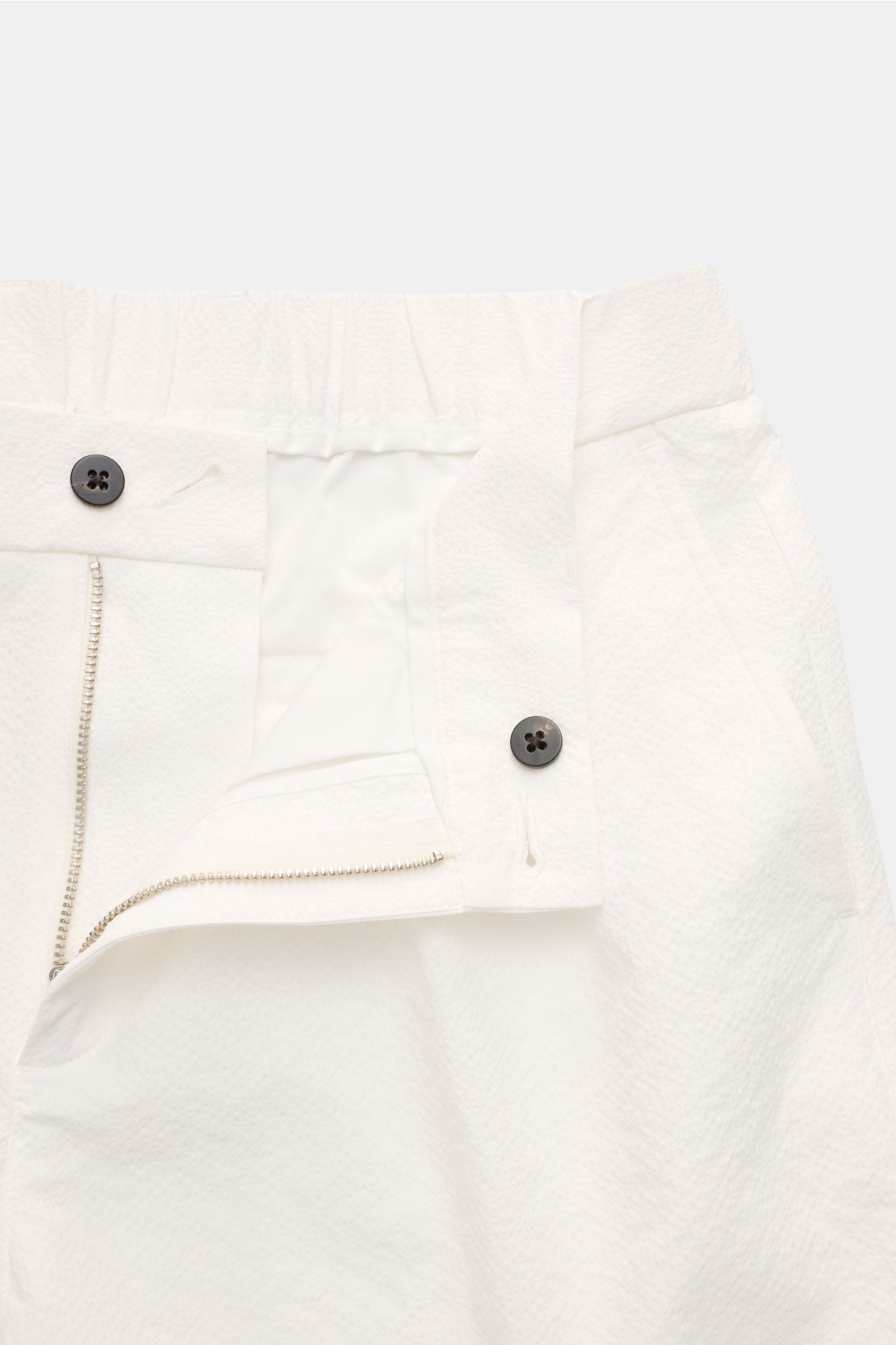 Close-up front view of 04651/ A trip in a bag Seersucker shorts white, showing zipper, button, and textured seersucker microfiber fabric.