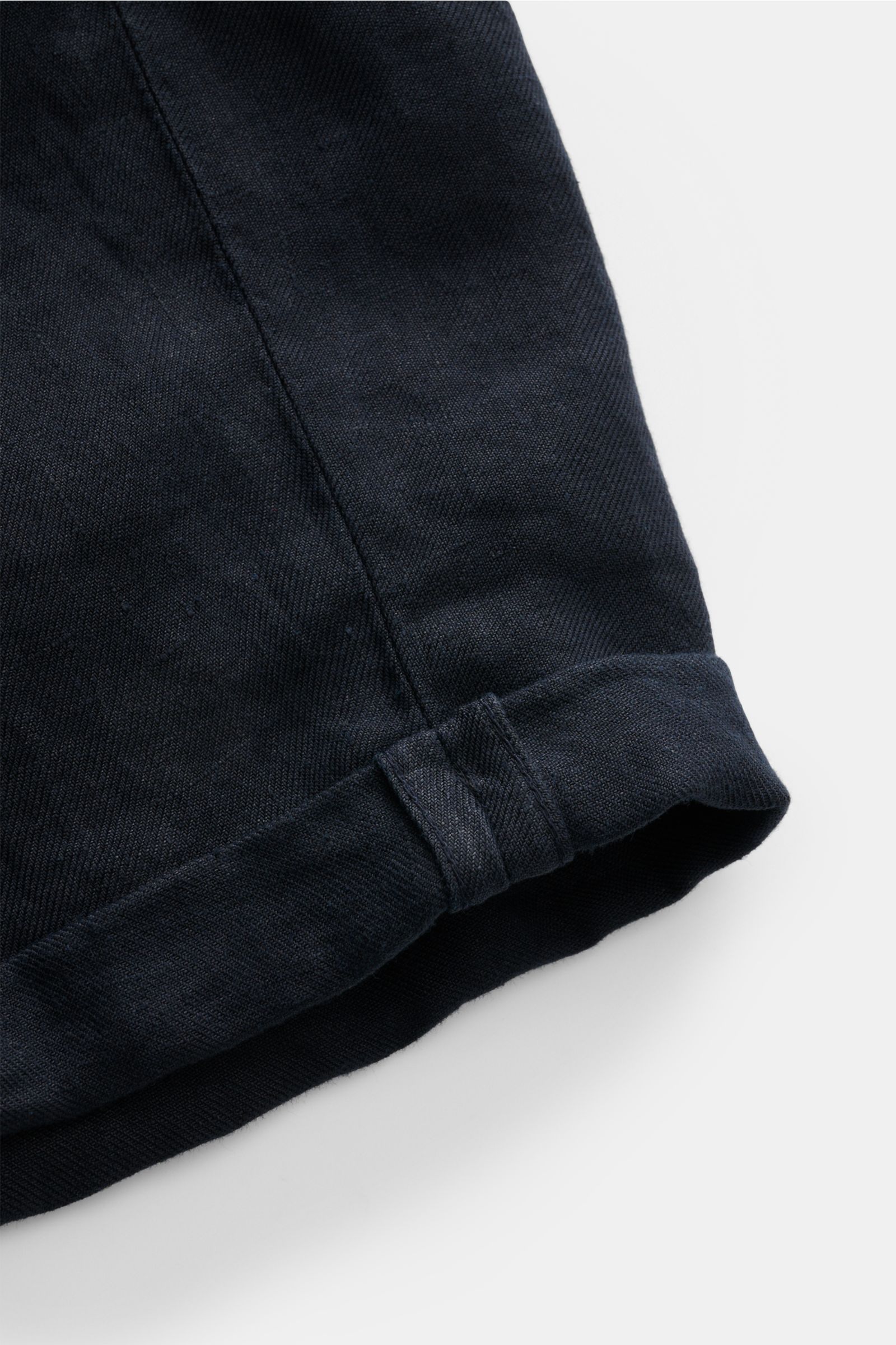 Close-up detail of the hem and fabric texture of Brunello Cucinelli Bermudas navy, photographed from above, highlighting the pure linen material and soft feel. Souveräne Sommer-Eleganz: Die Bermudas von BRUNELLO CUCINELLI verbinden hohen Tragekomfort m