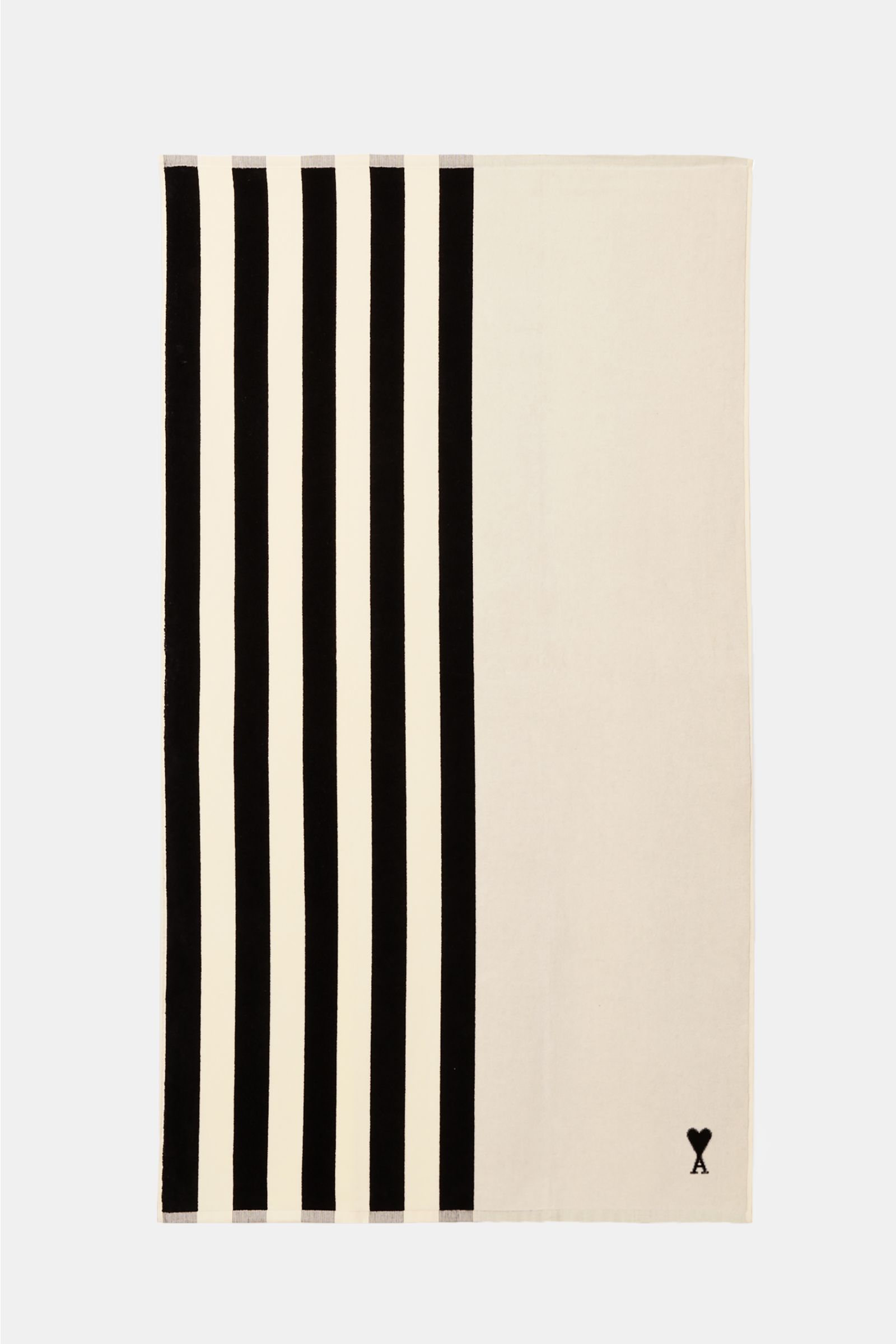 Ami Paris Strandtuch schwarz/weiß gestreift shown from above, featuring vertical black and white stripes on one side and solid white on the other with a small black logo. Luxuriöser Begleiter für sonnige Tage: Mit seinem ikonischen Streifendesign und d