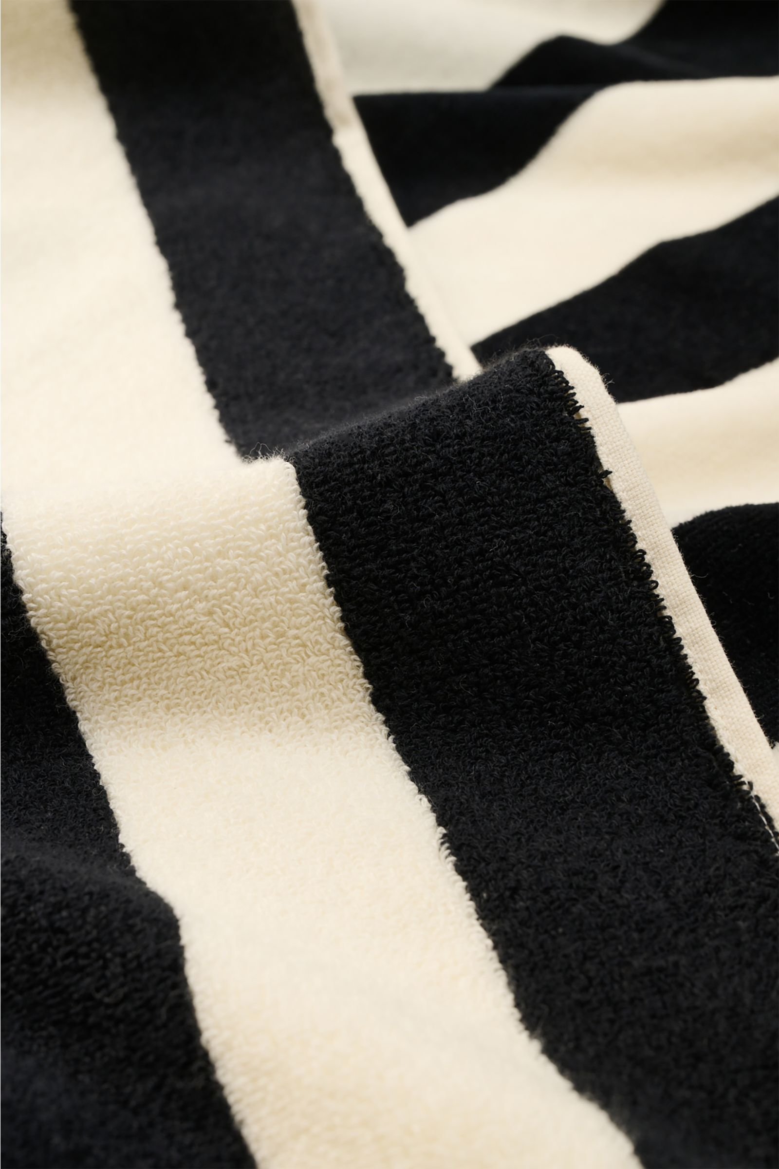 Close-up front view of Ami Paris Strandtuch schwarz/weiß gestreift beach towel showing soft cotton terry texture and bold stripes.

Luxuriöser Begleiter für sonnige Tage: Mit seinem ikonischen Streifendesign und der soften Baumwoll-Frottée-Qualität wir