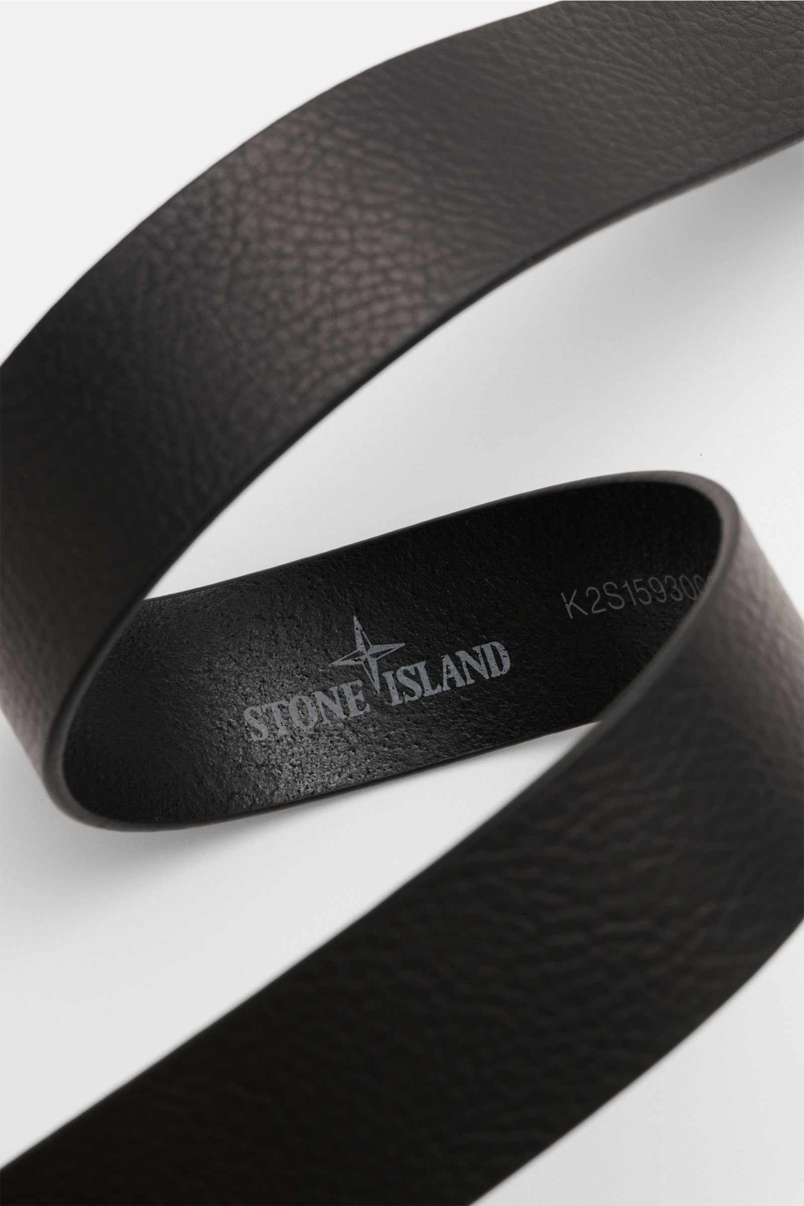 Stone Island Gürtel schwarz aus edlem Rindsleder mit charakteristischer Narbung, mattschwarzer Dornschließe, Durchzugschlaufe, Logo-Prägung, kleinem Weblabel, Made in Italy, Breite 4 cm, schräg von oben fotografiert.