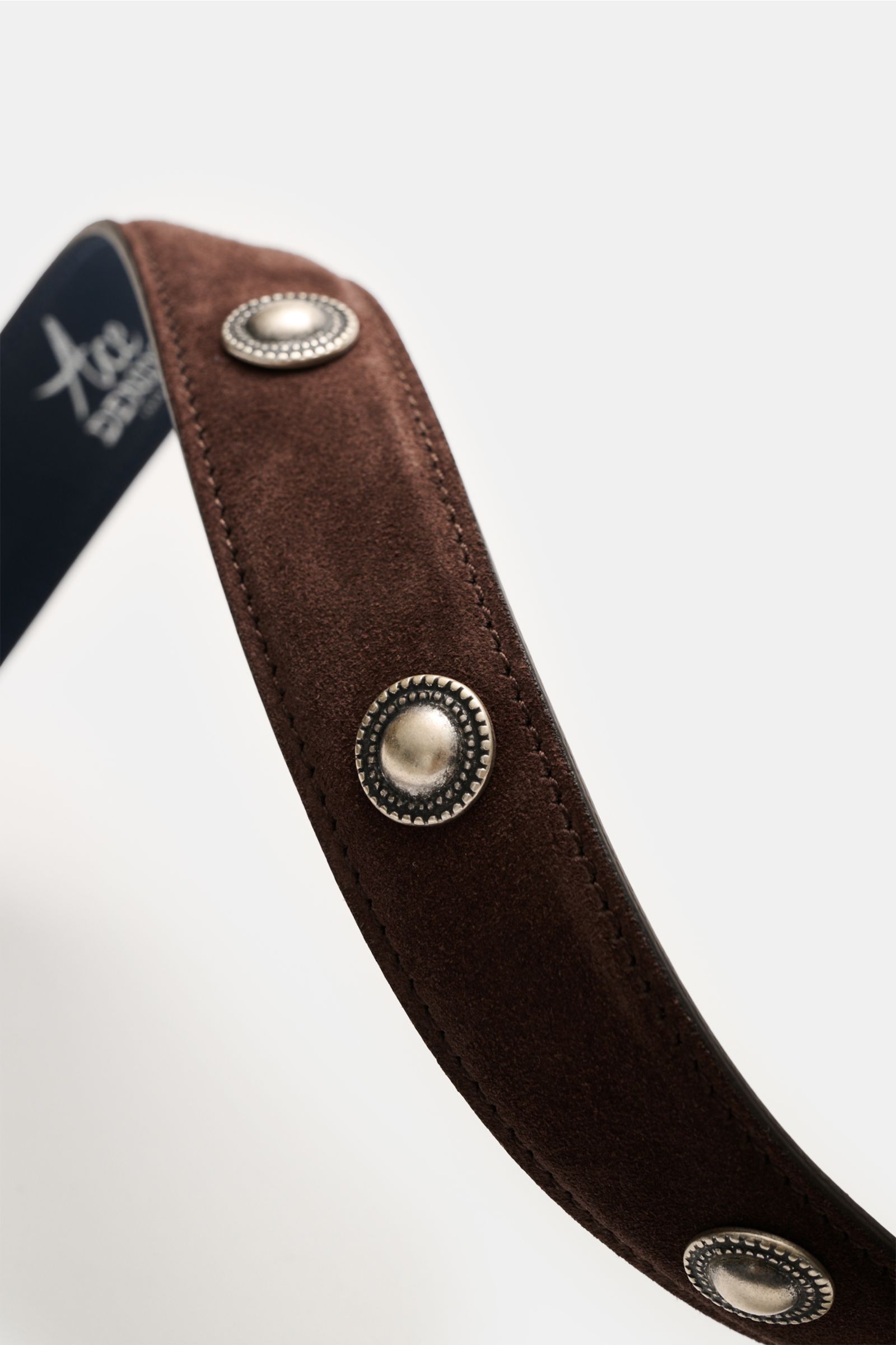 Ace Denim Veloursleder Gürtel 'Cowboy Belt' dunkelbraun shown from a close-up side angle, highlighting soft suede leather, silver Western-style conchos, detailed metal studs, and inner logo print; features silver buckle, metal belt loop, decorative tip, a