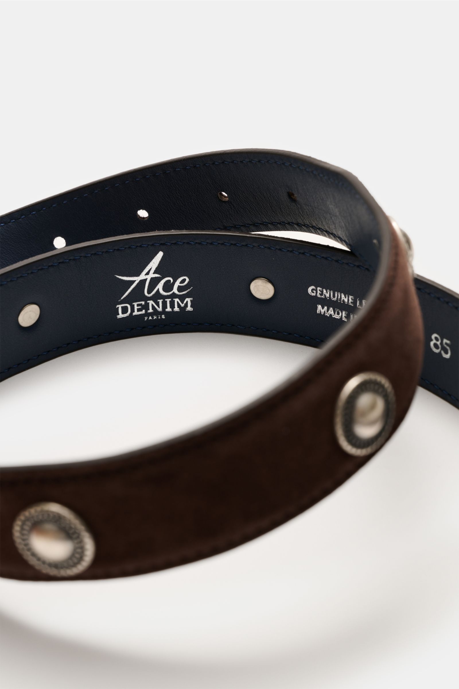 Close-up top-down view of Ace Denim Veloursleder Gürtel 'Cowboy Belt' dunkelbraun showing soft dark brown suede, silver conchos in Western style, metal belt loop, decorative metal tip, and embossed interior with logo, genuine leather, made in Italy, width