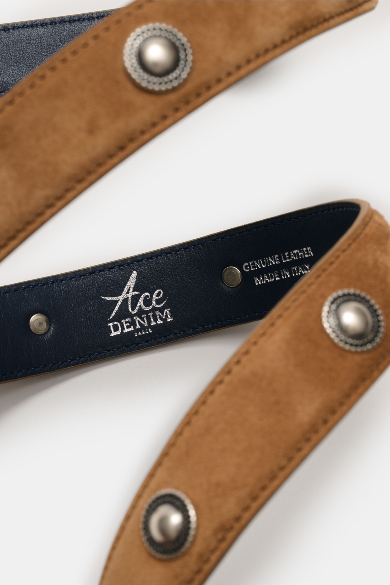 Close-up top view of Ace Denim Veloursleder Gürtel 'Cowboy Belt' hellbraun showing soft light brown suede with Western-style conchos, silver metal studs, and dark blue leather inner lining stamped 'GENUINE LEATHER MADE IN ITALY,' highlighting decorative m