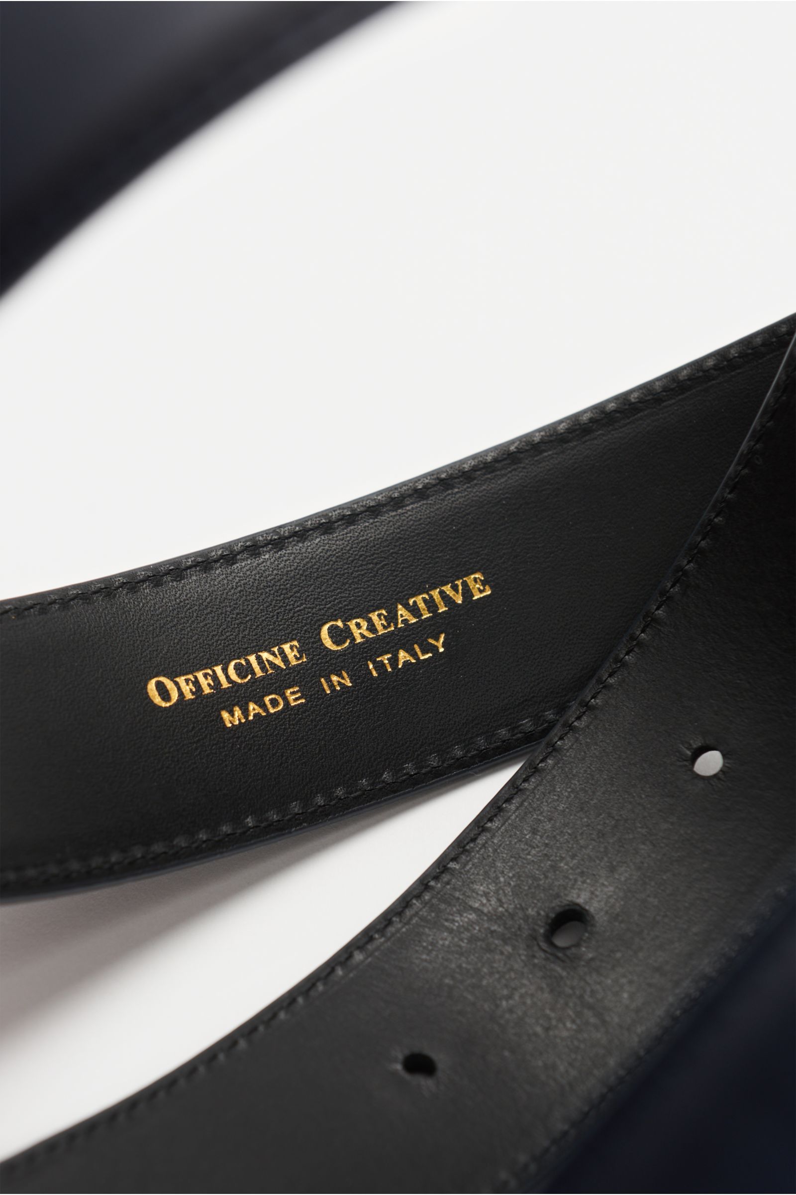 Close-up top view of the Officine Creative Gürtel navy showing smooth black leather with gold 'Officine Creative Made in Italy' embossing and belt holes.

Eleganter Akzentgeber: Der Gürtel von OFFICINE CREATIVE überzeugt mit seinem zeitlosen Design und