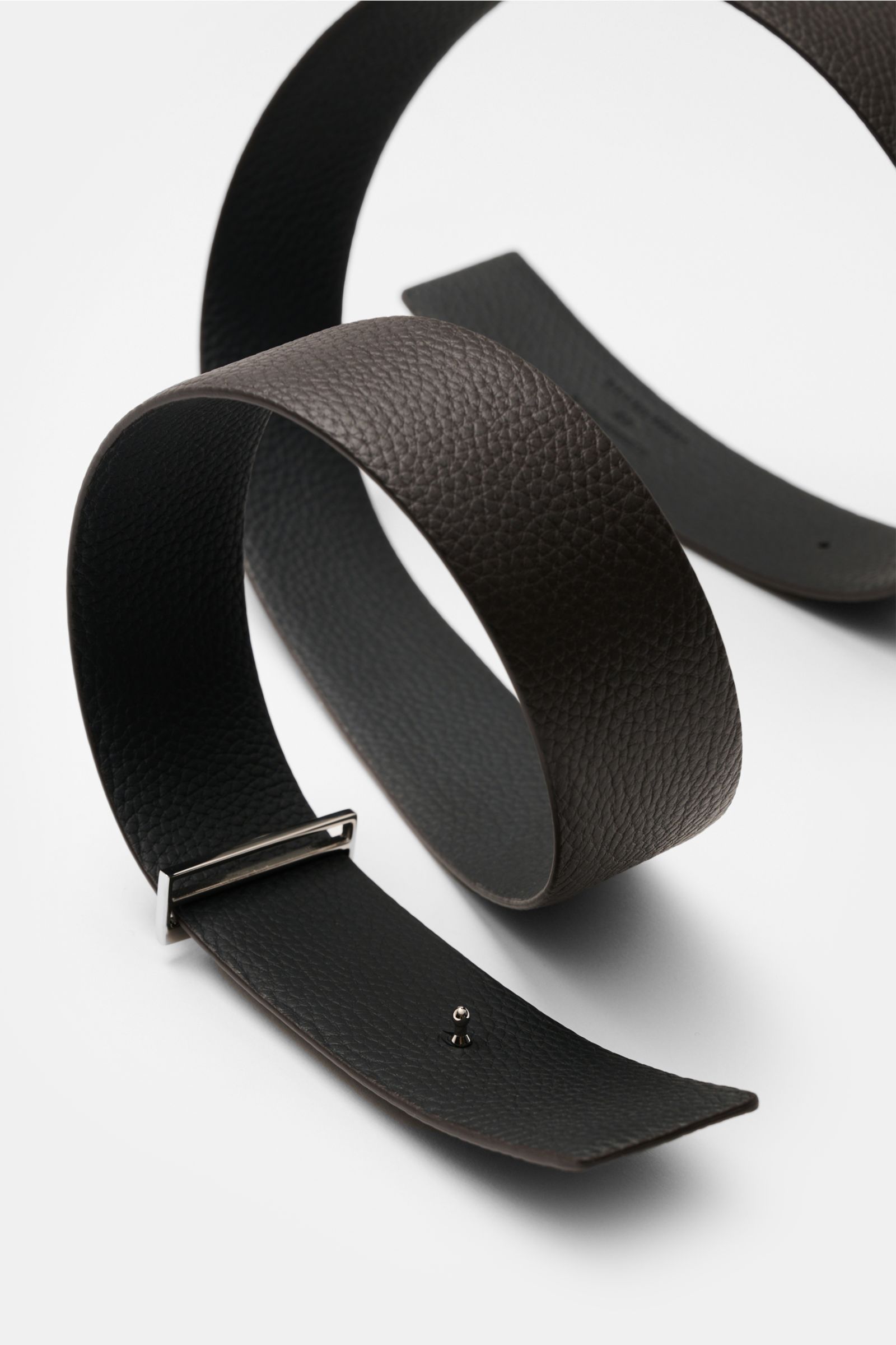 Close-up perspective of Tom Ford Gürtel schwarz/dunkelbraun displaying elegant reversible black and dark brown grained calf leather with silver brass buckle, width approx. 3.5 cm, made in Italy.

Description incorporated:  
Eleganter Eyecatcher: Mit se