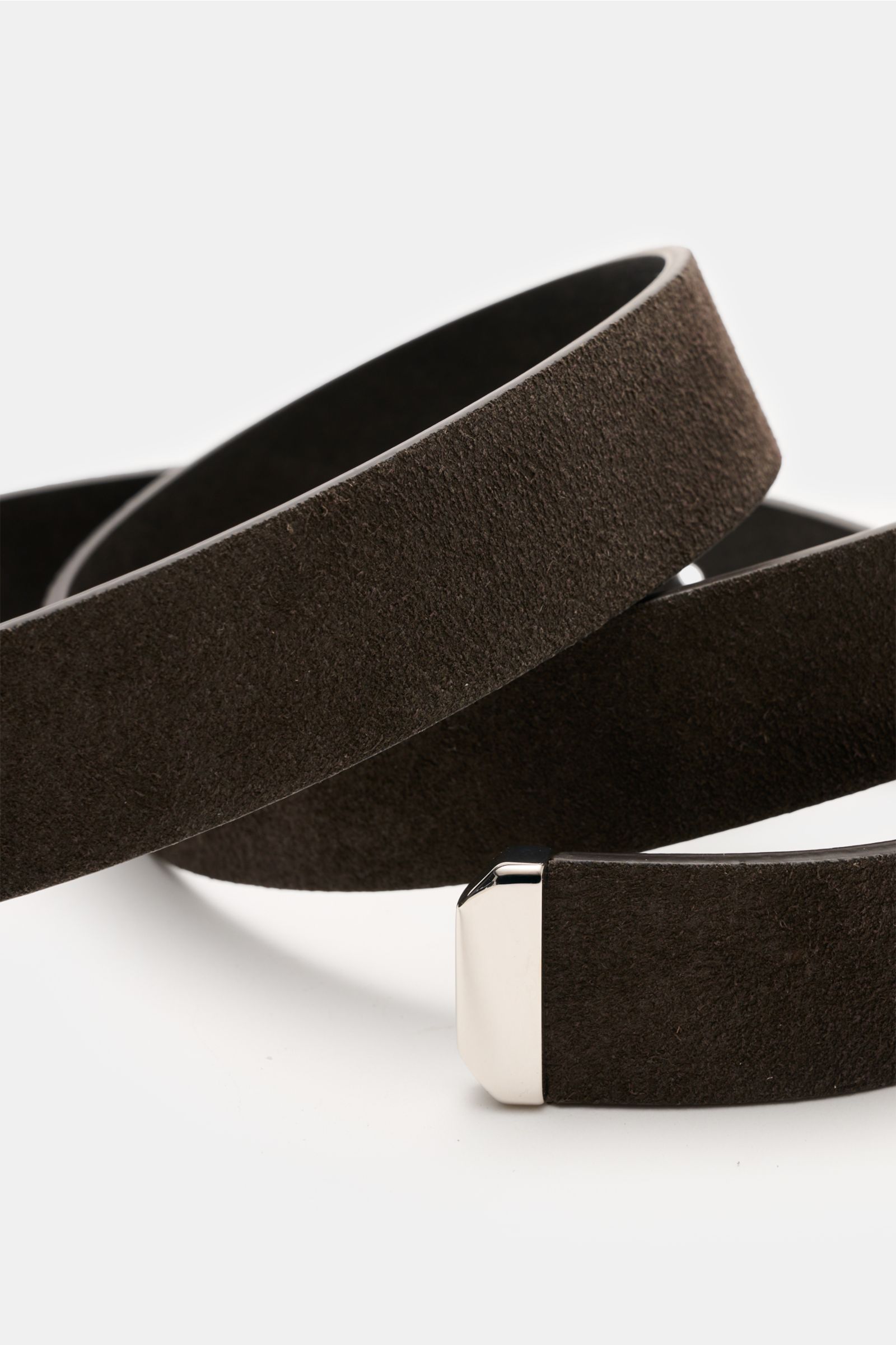 Brunello Cucinelli Veloursleder Gürtel dunkelbraun aus softem Veloursleder, silberfarbener Dornschließe, eine Durchzugschlaufe, ca. 3 cm breit, Made in Italy, nah aus schräger Perspektive fotografiert.