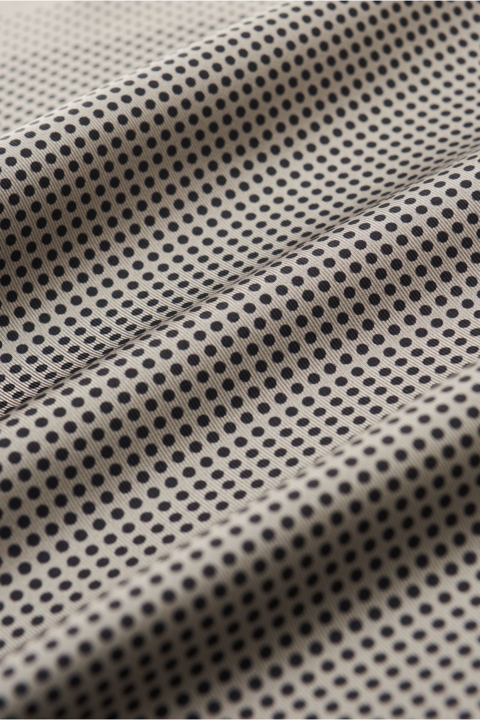 Tom Ford Einstecktuch grau/schwarz gepunktet aus reiner Seide mit geschmeidigem Griff, modernem Punkte-Design, handrollierten Kanten, kleinem TOM FORD-Logo, Made in Italy, Maße 40x40 cm, aus schräger Nahaufnahme fotografiert.