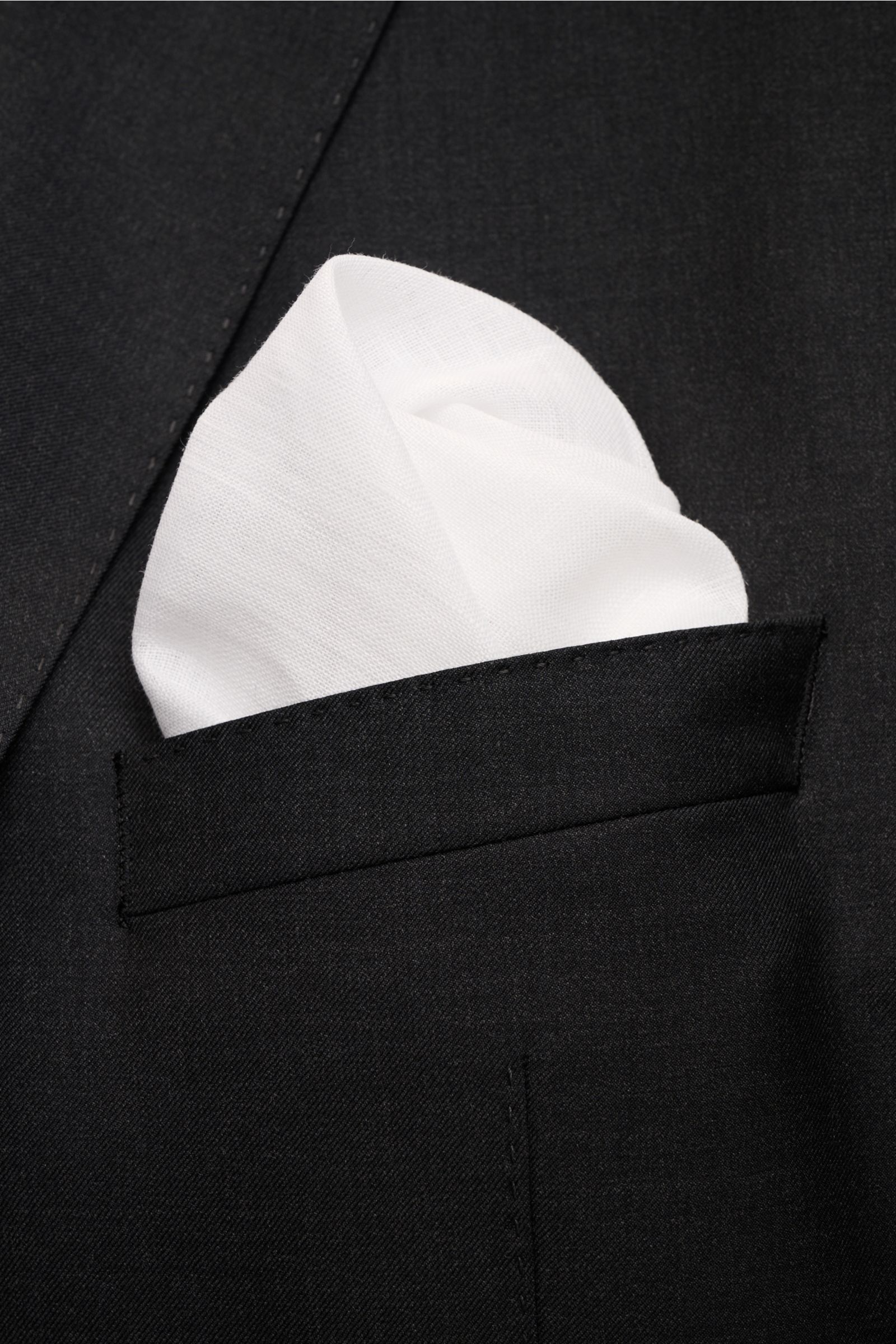 Rosi Collection Einstecktuch 'One' weiß aus reinem Leinen mit rollierten Kanten, fotografiert in Nahaufnahme in der Brusttasche eines schwarzen Sakkos.
