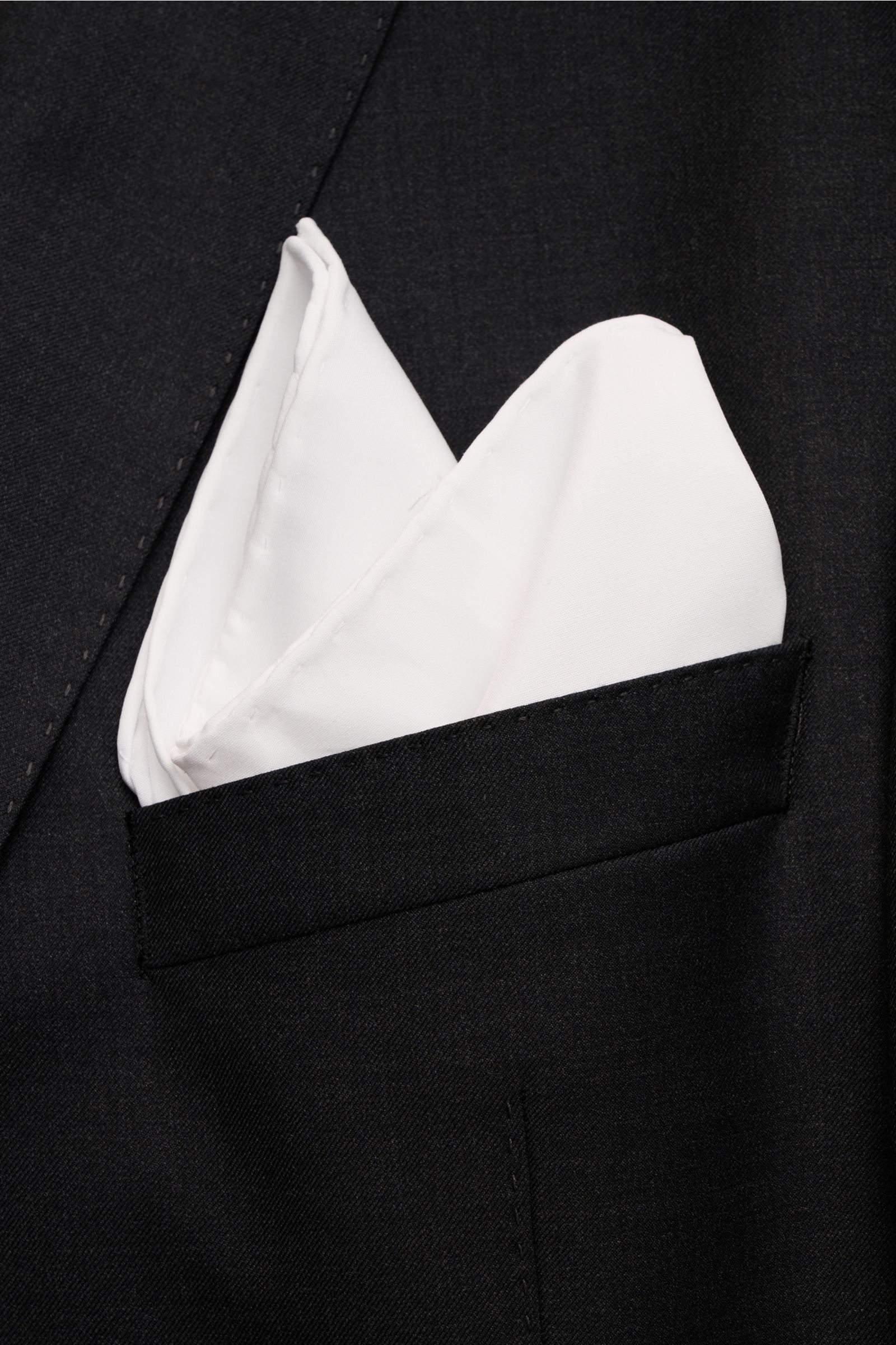 Rosi Collection Einstecktuch 'One' weiß aus reiner Baumwolle mit rollierten Kanten, elegant gefaltet in schwarzem Sakko, seitliche Nahaufnahme.