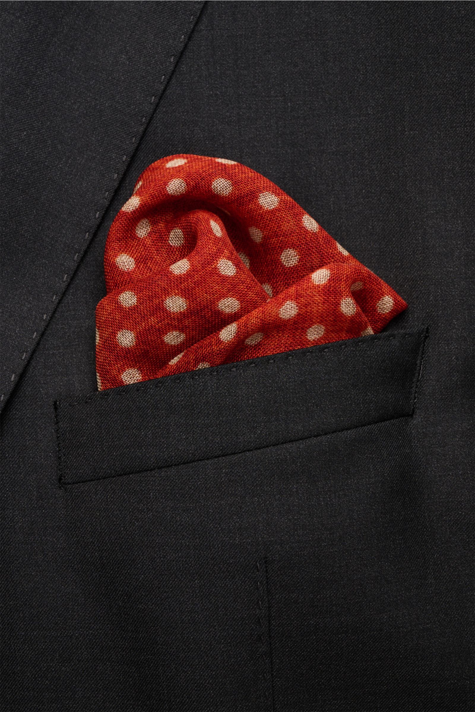 Rosi Collection Einstecktuch rostbraun/beige gepunktet in schwarzer Jackettasche, reine Wolle, weicher Griff, grafisches Punktmuster, handrollierte Kanten, Made in Italy, ca. 29x29 cm, Nahaufnahme frontale Perspektive.