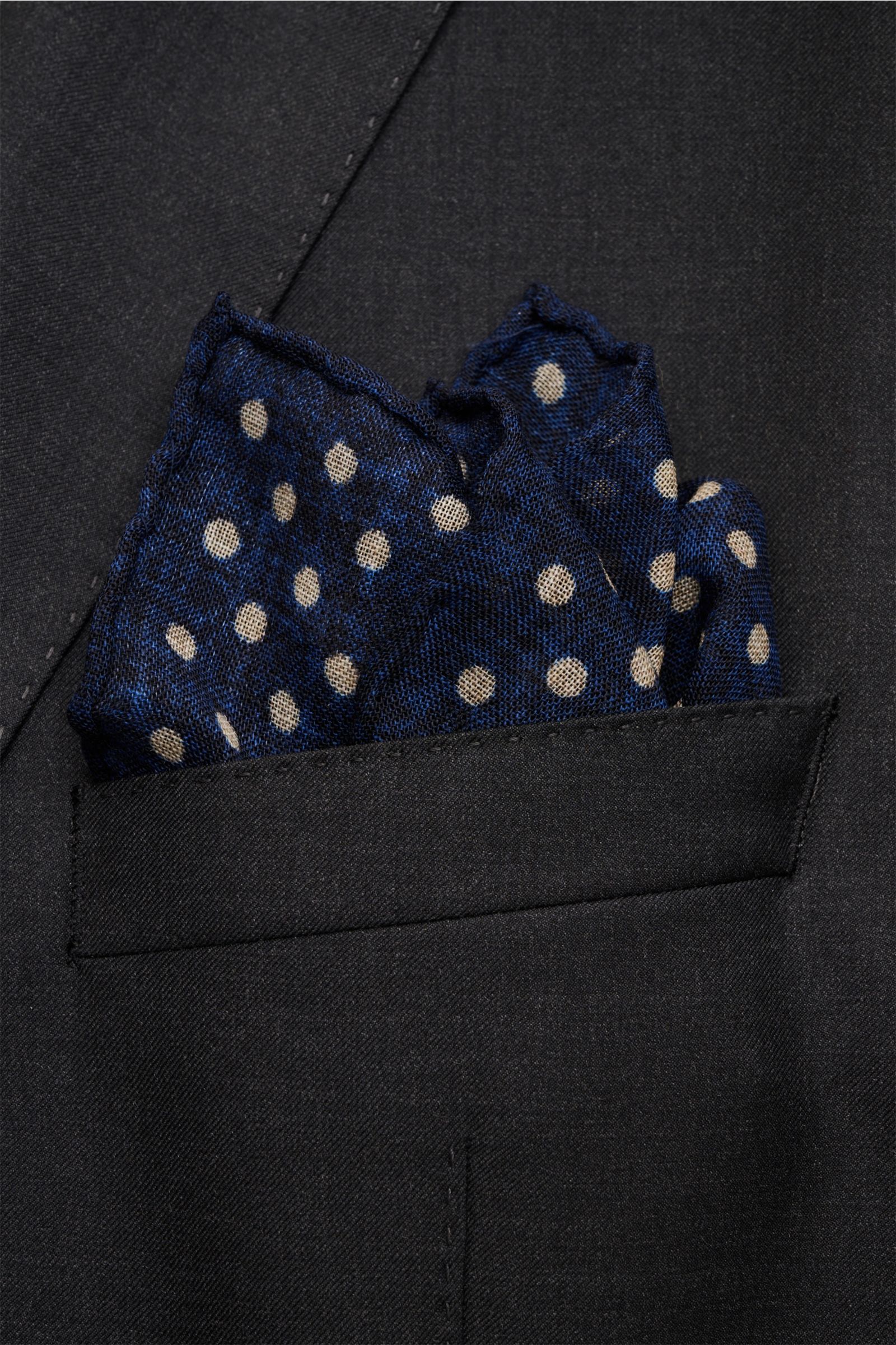 Rosi Collection Pocket square navy/beige dotted shown from a close-up front angle in a black jacket pocket, pure wool, soft feel, graphic polka dot pattern, hand-rolled edges, made in Italy, dimensions approx. 29 cm x 29 cm.