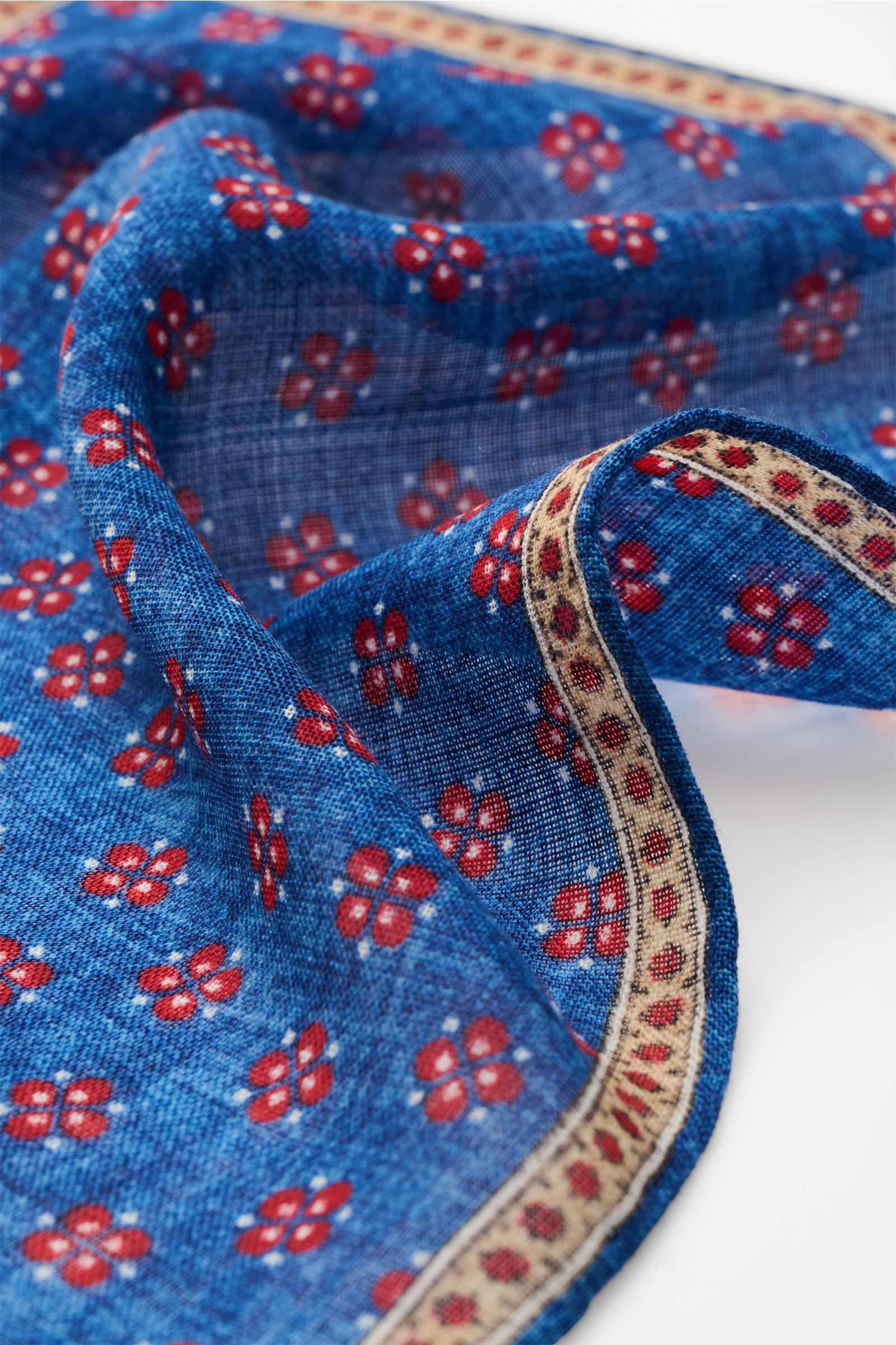 Rosi Collection Pocket square 'Ted' blue mottled/red/beige patterned, floral print with edging, rolled edges, pure wool, photographed close-up from an angled top view.  
Elegant and eye-catching: With its floral pattern, this pocket square in pure wool