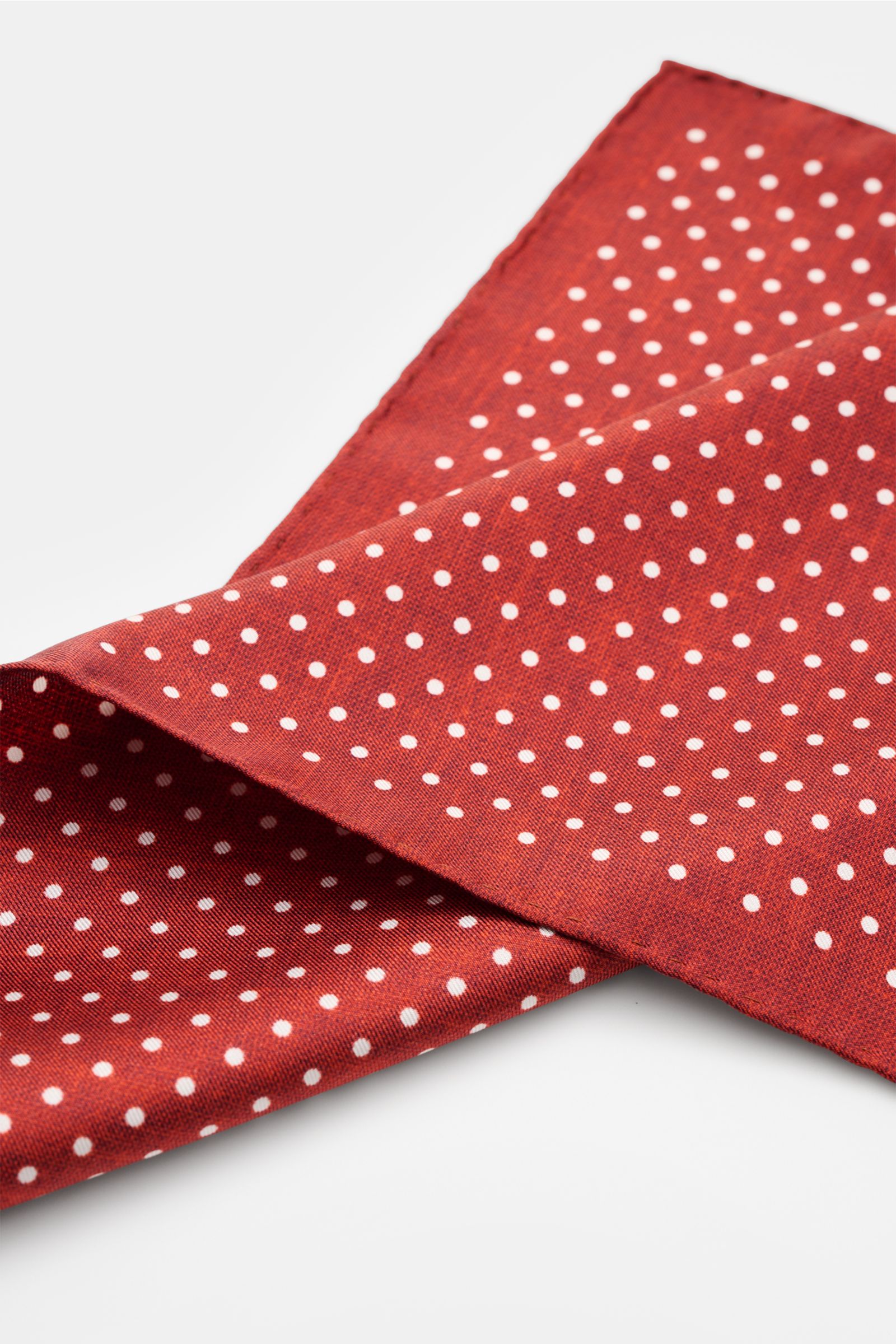 Rosi Collection Seiden-Einstecktuch dunkelrot gepunktet, reine Seide, geschmeidiger Griff, grafisches Punktmuster, handrollierte Kanten, Made in Italy, ca. 31x31 cm, nah von schräg oben fotografiert.