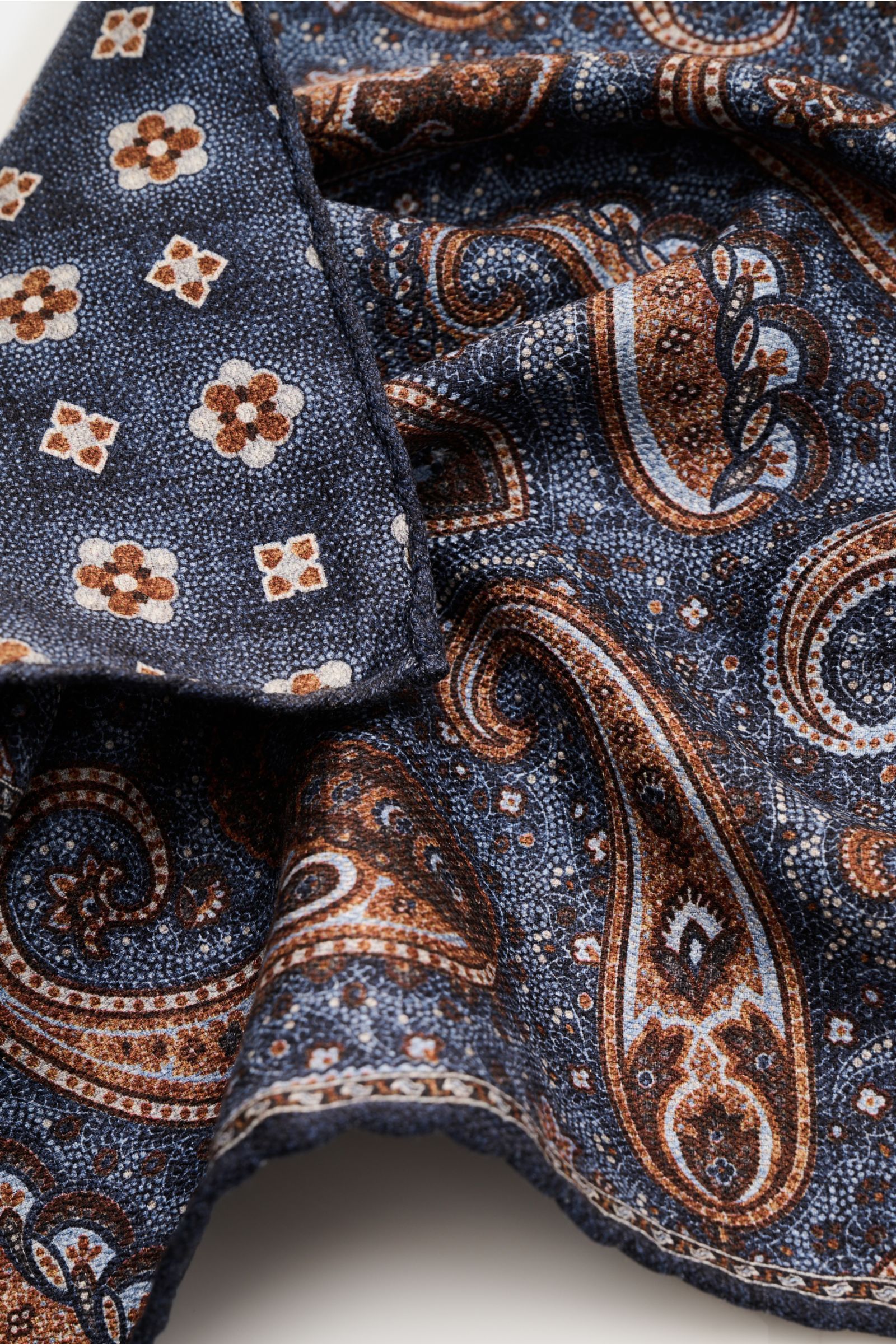 Rosi Collection Seiden-Einstecktuch 'Easy' graublau/hellblau/braun gemustert, Paisley-Muster mit Borte, Medaillon-Rückseite, handrollierte Kanten, reine Seide, soft, 31x31 cm, Made in Italy, Nahaufnahme von schräger Perspektive.