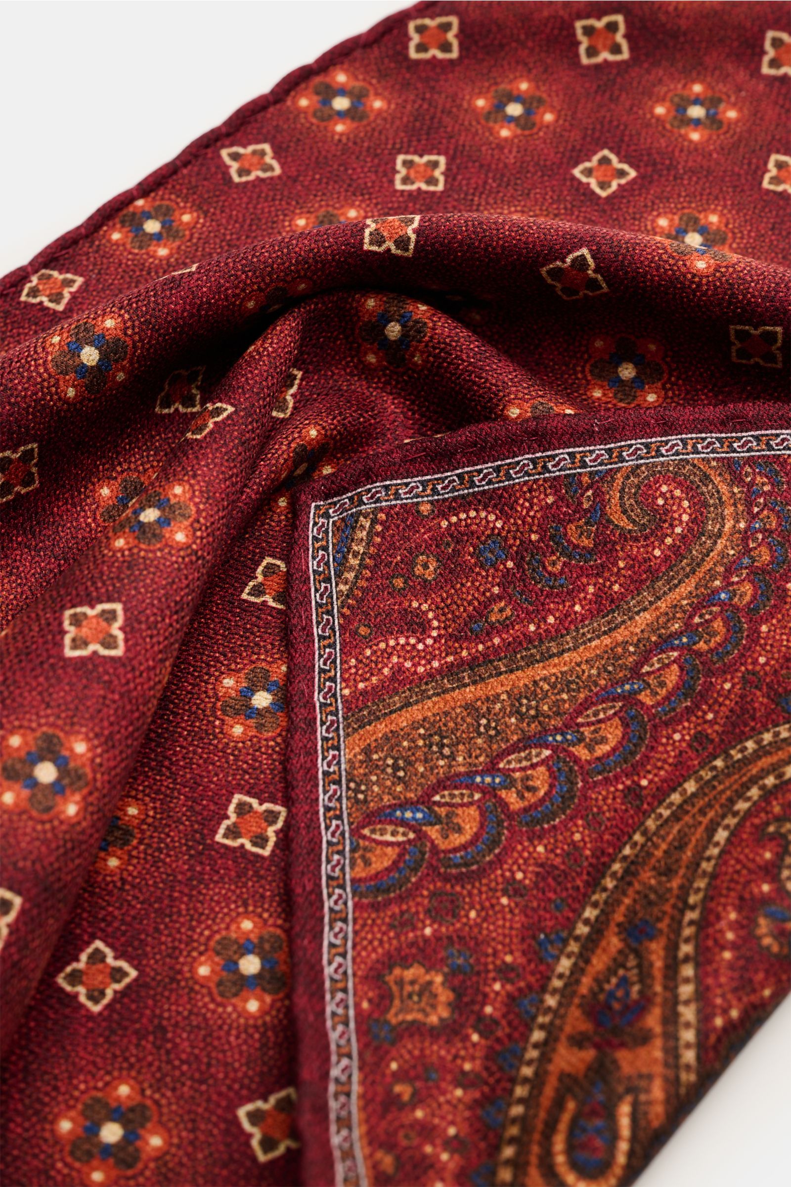 Rosi Collection Seiden-Einstecktuch 'Easy' bordeaux/orange/blau gemustert, aus reiner Seide mit softem Griff, Paisley-Muster und handrollierten Kanten, Rückseite Medaillon-Muster, Made in Italy, 31x31 cm, Nahaufnahme schräg von oben.
