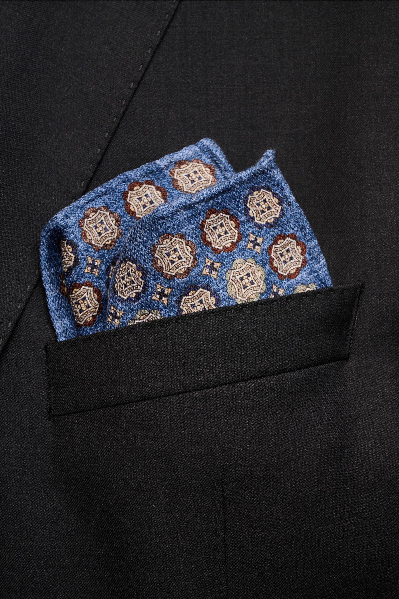Rosi Collection Seiden-Einstecktuch 'Easy' blau/braun/graugrün gemustert, reine Seide, Medaillon-Print, Paisley-Rückseite, handrollierte Kanten, soft, Made in Italy, ca. 30,5x30,5 cm, von schräg oben im schwarzen Sakko steckend.