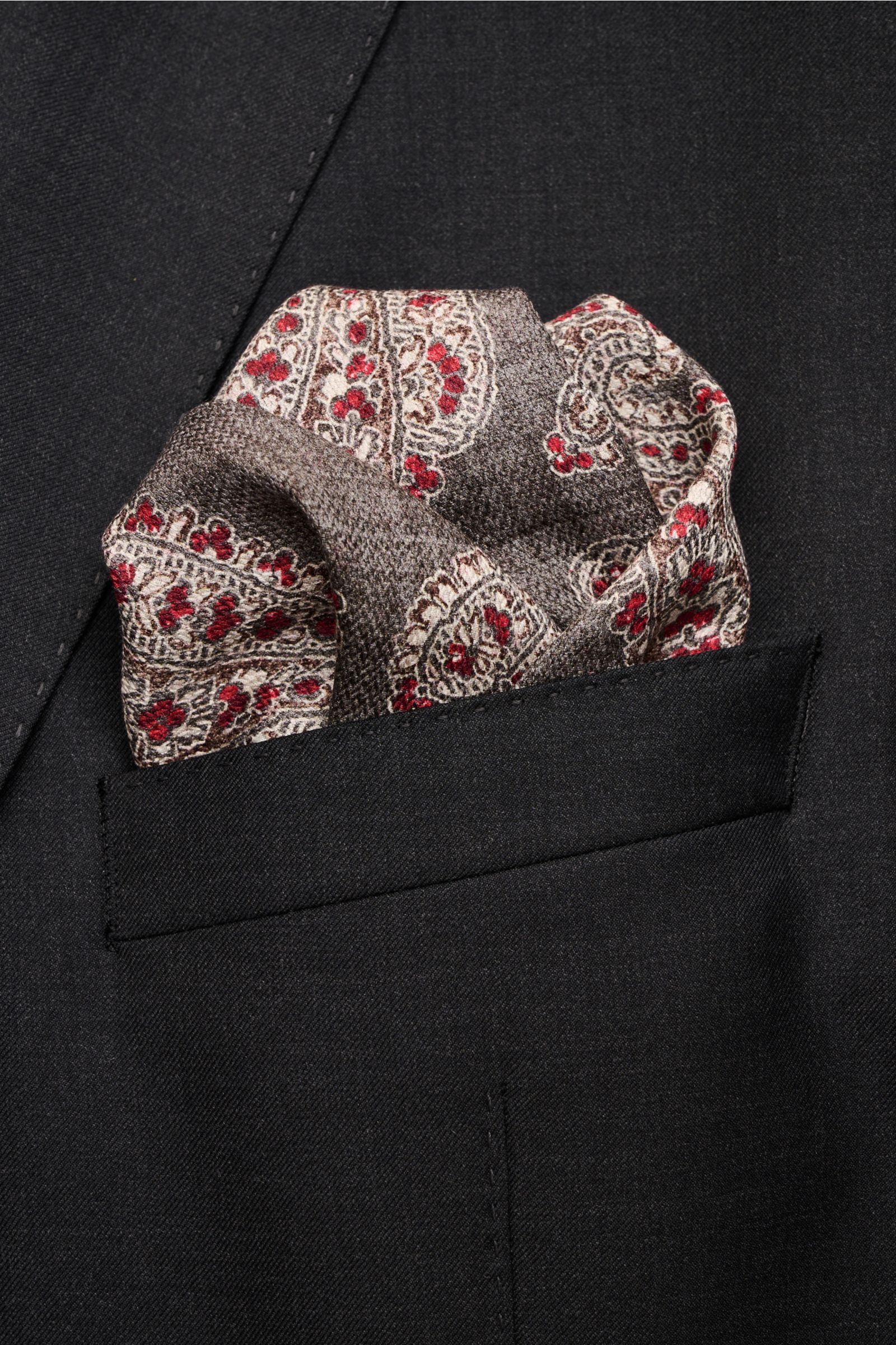 Rosi Collection Seiden-Einstecktuch 'Easy' grau/dunkelrot/dunkelbraun gemustert aus reiner Seide mit Paisley-Muster, Borte, Kachel-Rückseite, rollierte Kanten, Maße 31x31 cm, Made in Italy, fotografiert in Frontansicht steckend in schwarzer Sakko-Brusttas