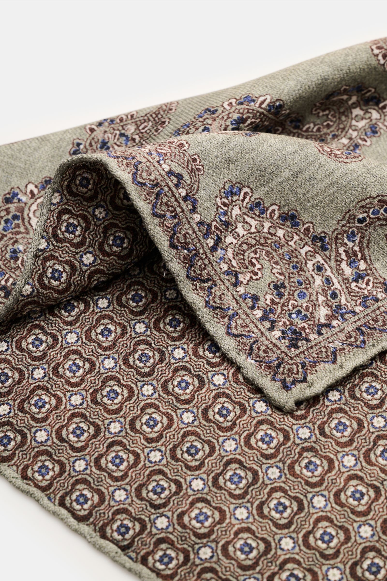 Rosi Collection Seiden-Einstecktuch 'Easy' graugrün/dunkelbraun/dunkelblau gemustert, weich, Paisley-Muster mit Borte, Rückseite Kachel-Muster, rollierte Kanten, reine Seide, Maße 31x31 cm, Made in Italy, Nahaufnahme, seitliche Perspektive.