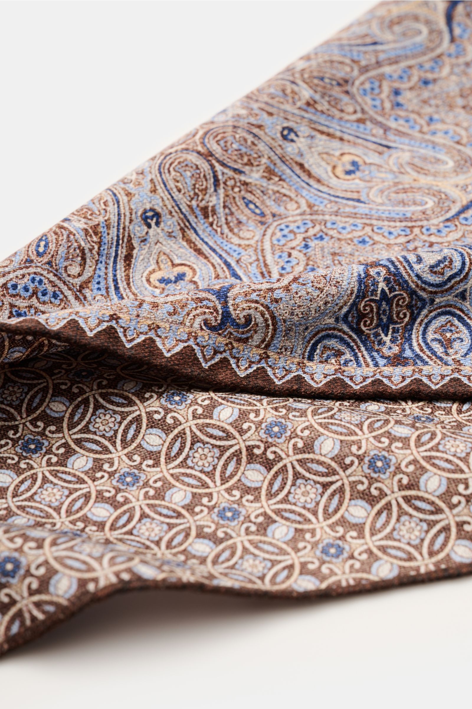 Rosi Collection Einstecktuch 'Easy' dunkelbraun/blau/weiß gemustert, aus reiner Seide mit modernem Paisley, Vorder- und Rückseite sichtbar, rollierte Kanten, ca. 31x31 cm, Made in Italy, Nahaufnahme schräg von oben.