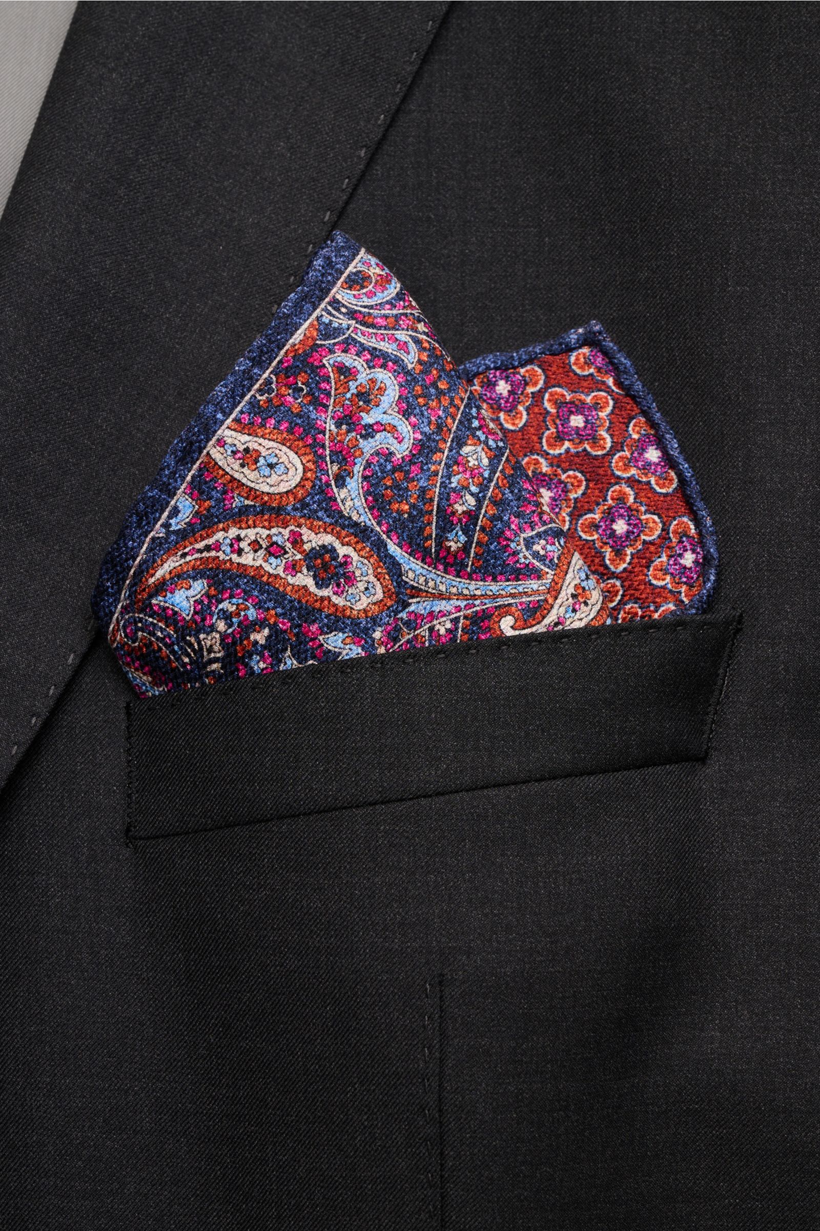Rosi Collection Seiden-Einstecktuch 'Easy' graublau/rostbraun/violett gemustert, reine Seide, Paisley- und Kachel-Muster, handrollierte Kanten, Made in Italy, 31x31 cm, in schwarzer Jackettasche von schräg oben fotografiert.