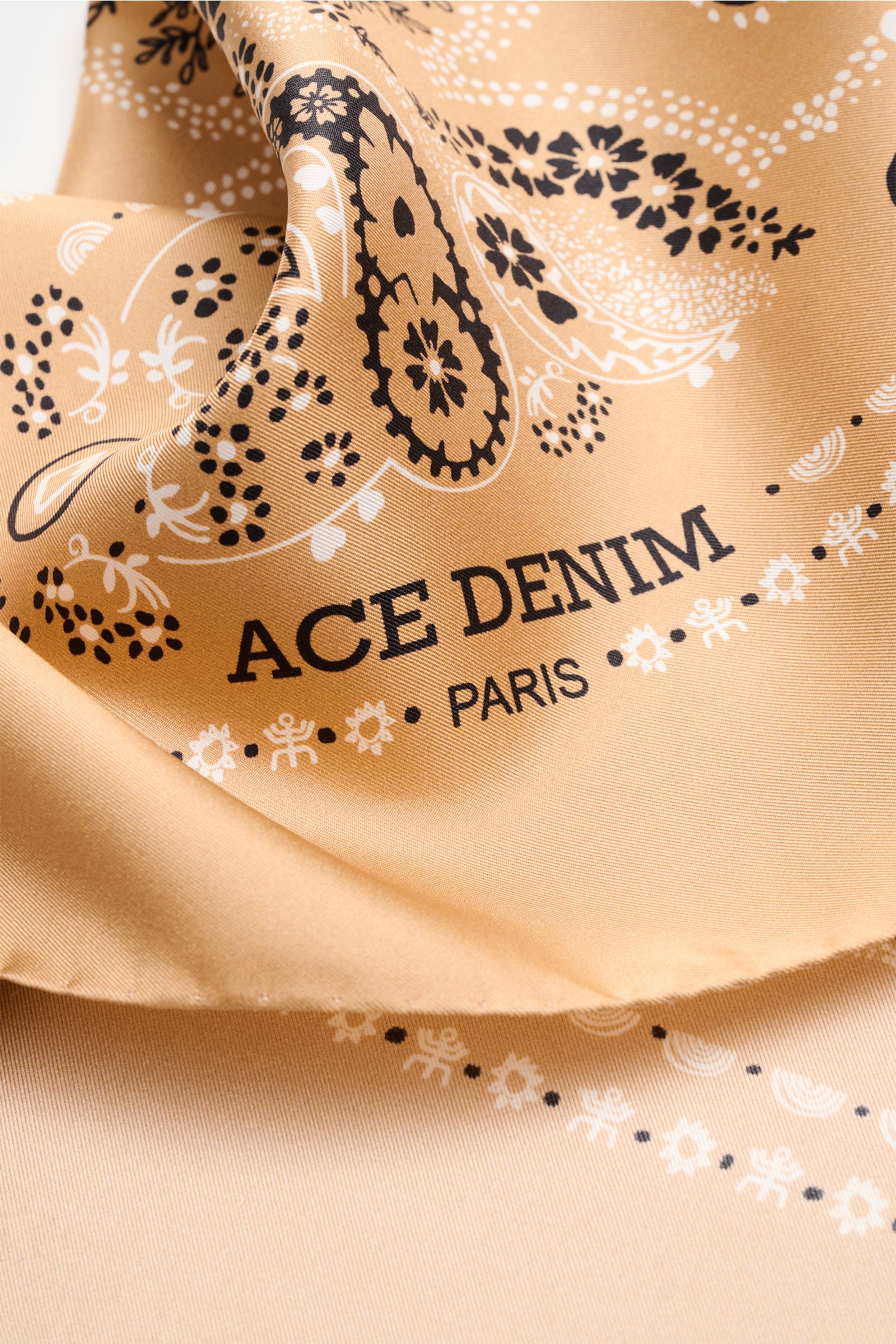 Close-up front view of the Ace Denim Silk scarf light brown/black/white patterned showing paisley design and 'ACE DENIM PARIS' text.

Eye-catching for the warm season: The ACE DENIM silk scarf in a bandana design is a casual statement accessory for sum